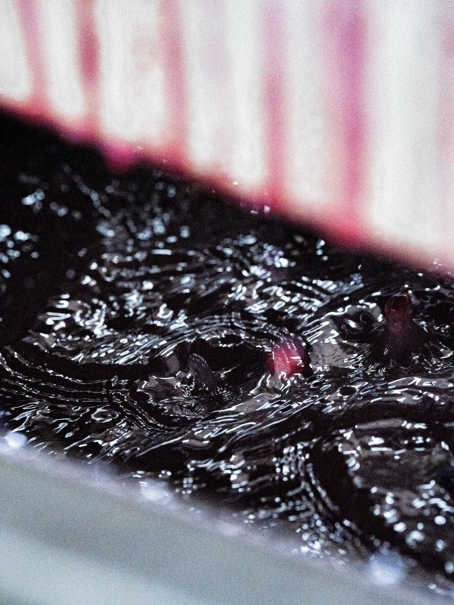 Gouttes de liquide noir avec des reflets, probablement du sirop de raisin, dans une cuve ou un récipient, avec une partie floue en haut et en bas.