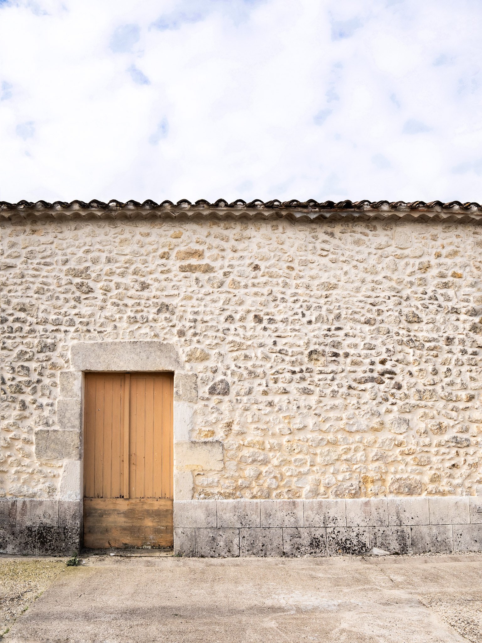 Mur en pierre avec une porte en bois, ciel nuageux en arrière-plan.
