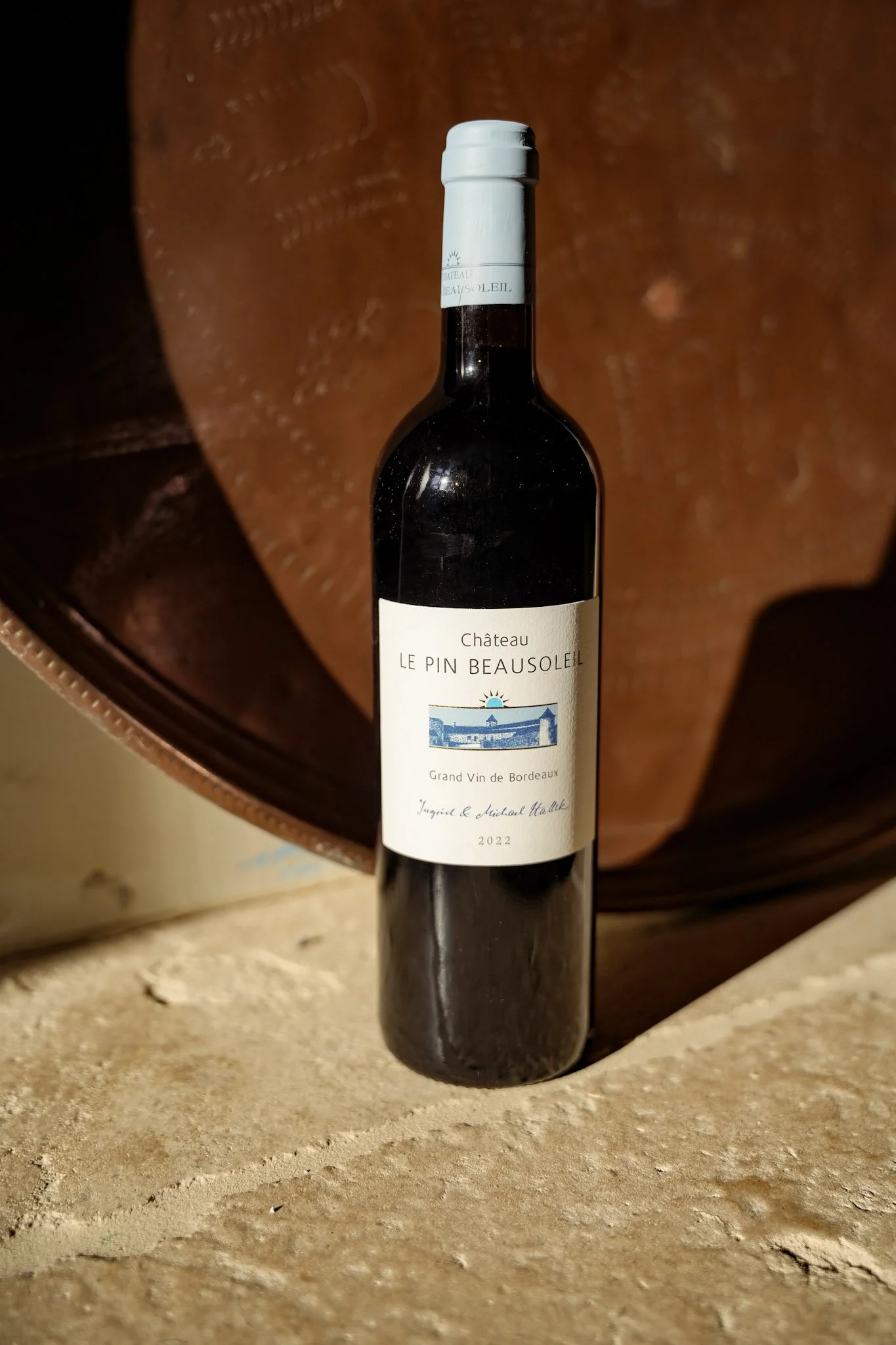 Une bouteille de vin rouge baptisée Château Le Pin Beausoleil, année 2022, posée sur une surface en pierre avec un arrière-plan en cuir.
