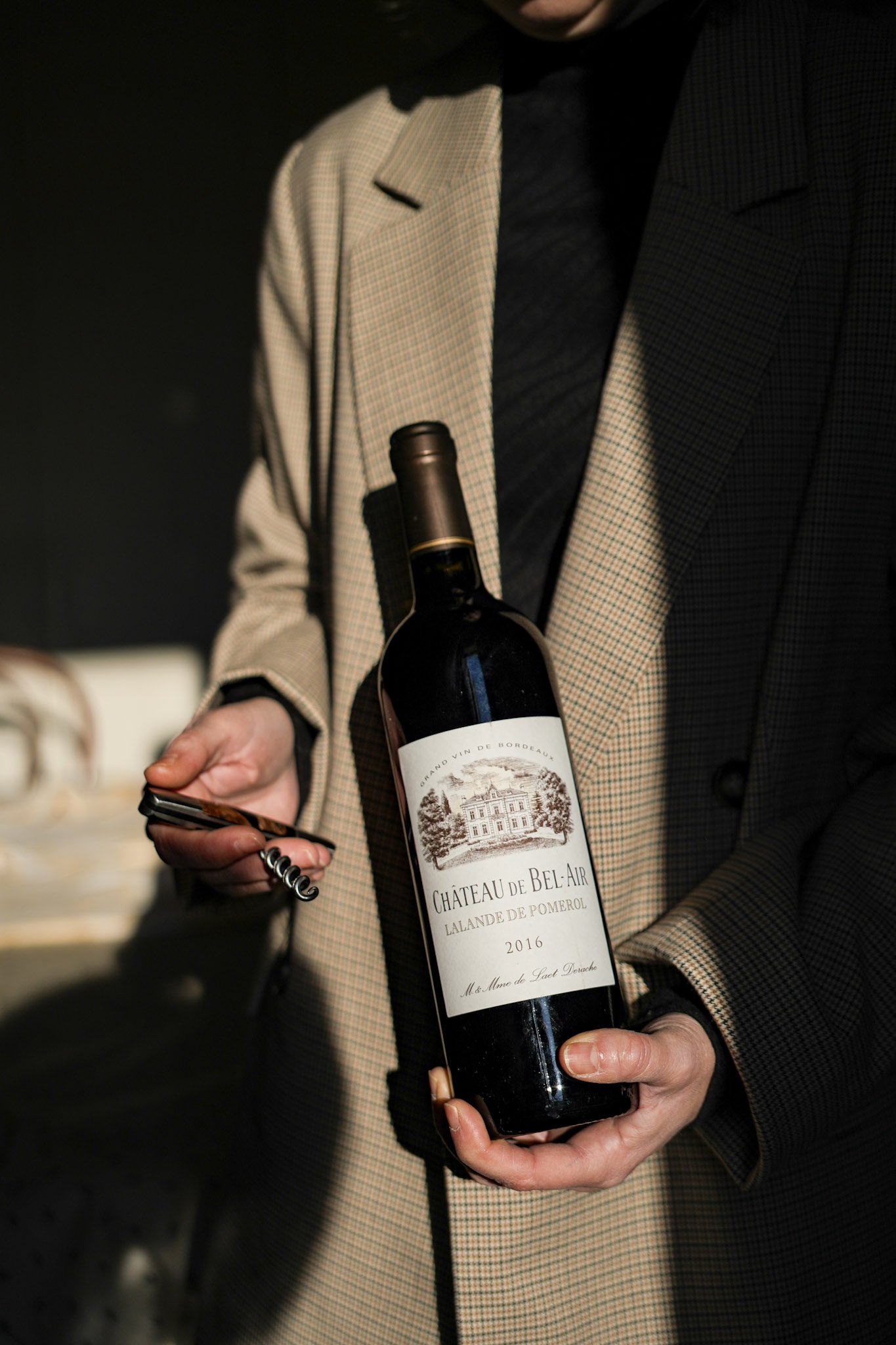 Personne tenant une bouteille de vin rouge Château Château de Bel-Air 2016 et un ouvre-bouteille.