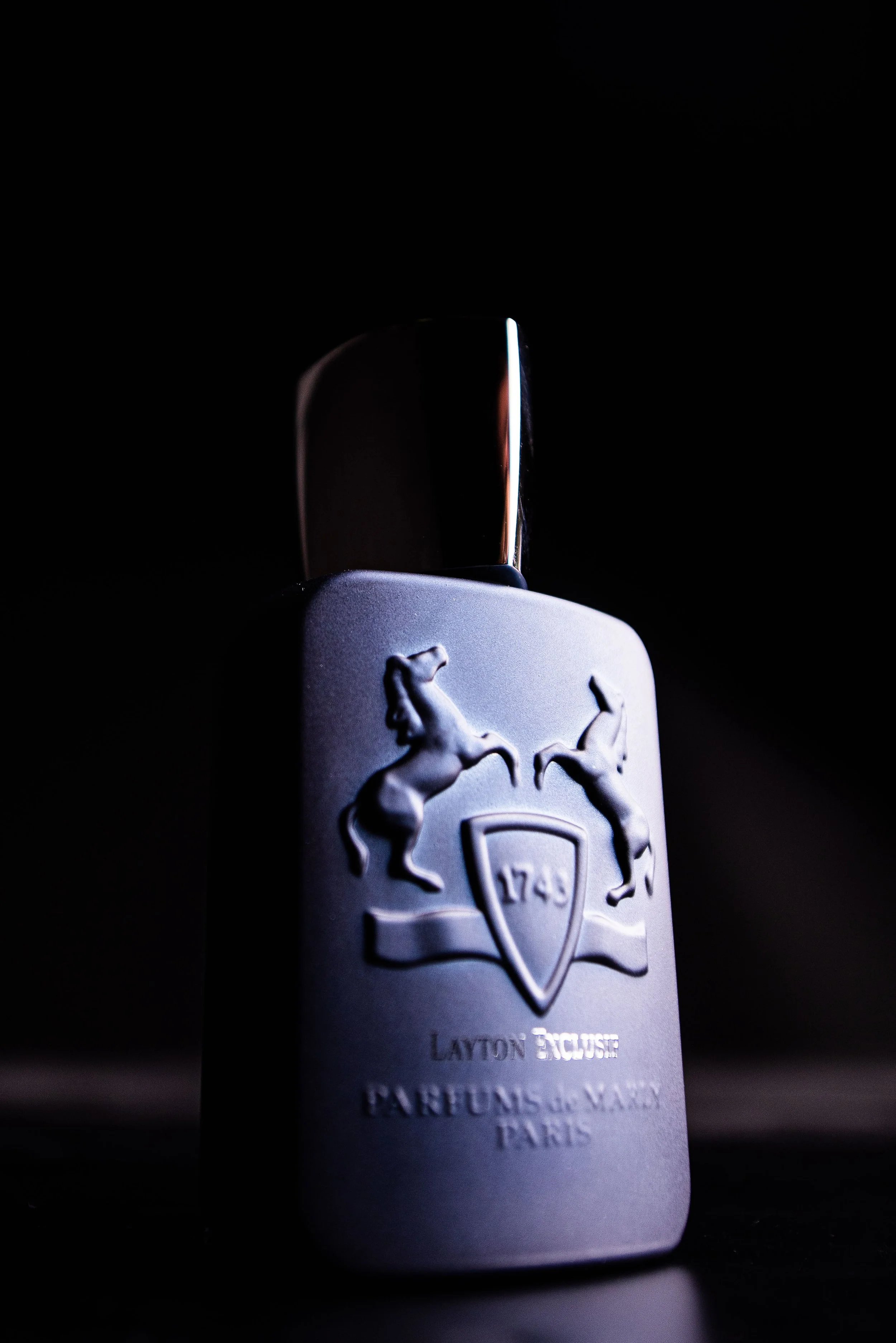 Dufthülle mit silbernem Deckel, graue Oberfläche, Pony-Emblem, Jahr 1749, Markenname 'Layton Exclusive Parfums de Marly Paris', vor dunklem Hintergrund.