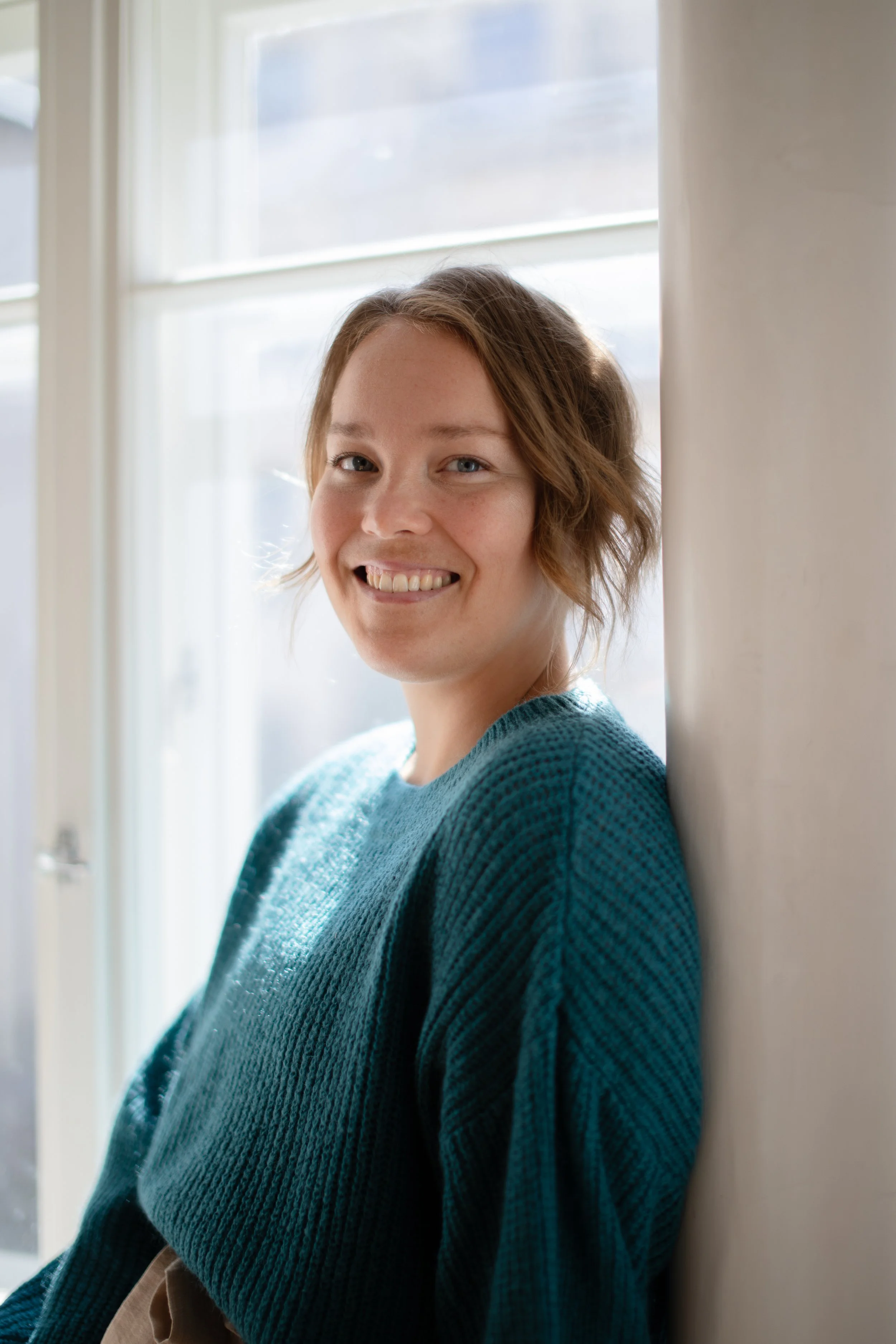 Oona istuu aurinkoisella ikkunalaudalla ja hymyilee.