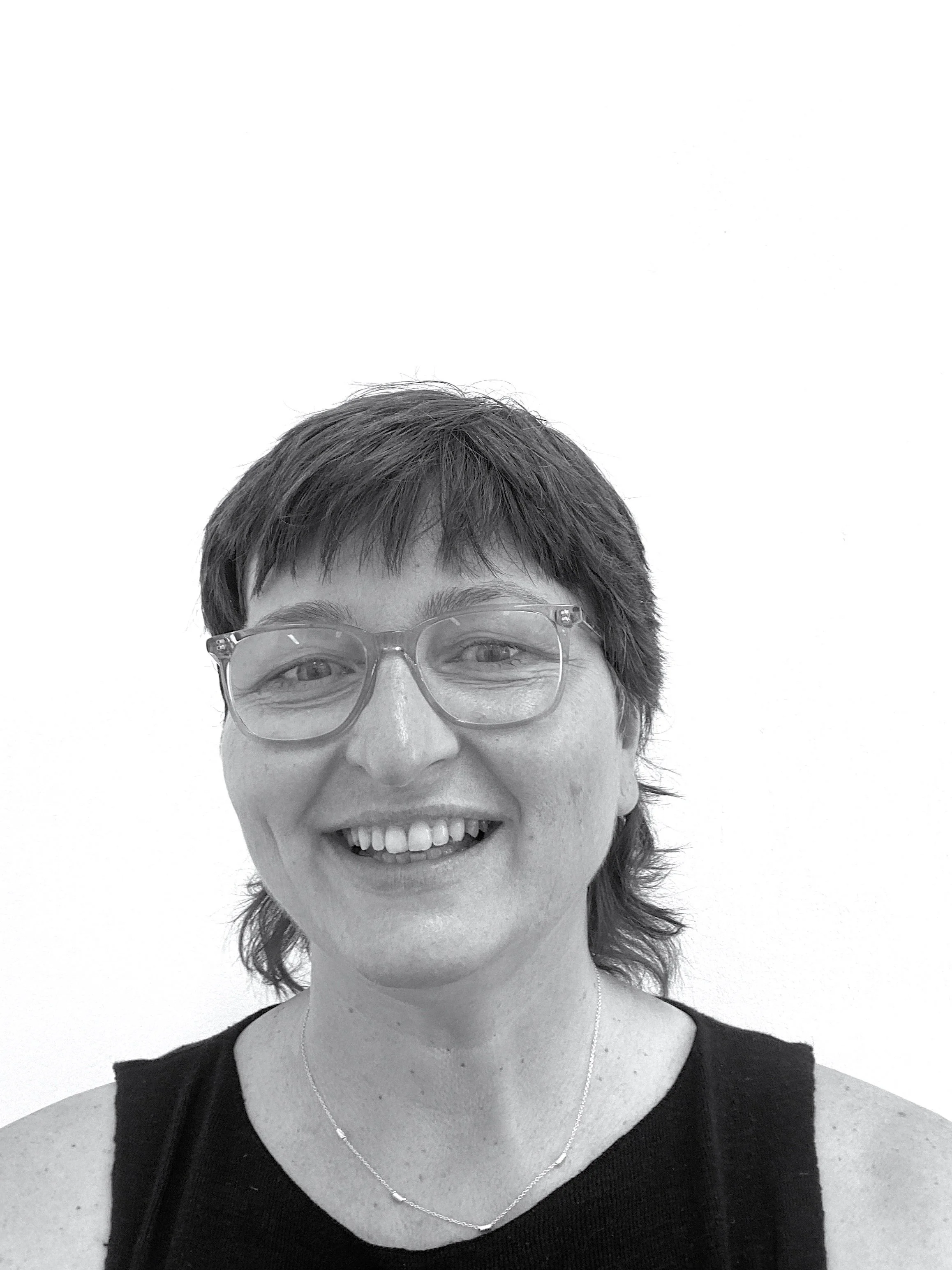 A woman with short, dark hair wearing glasses and a black sleeveless top, smiling at the camera.