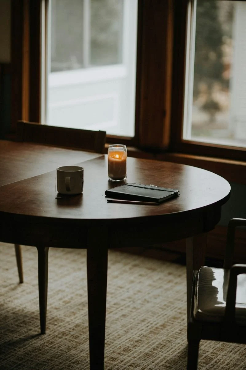 dining table with candle, cup with tea, and closed journal ready to be written in to represent setting goals and intentions for your day and year