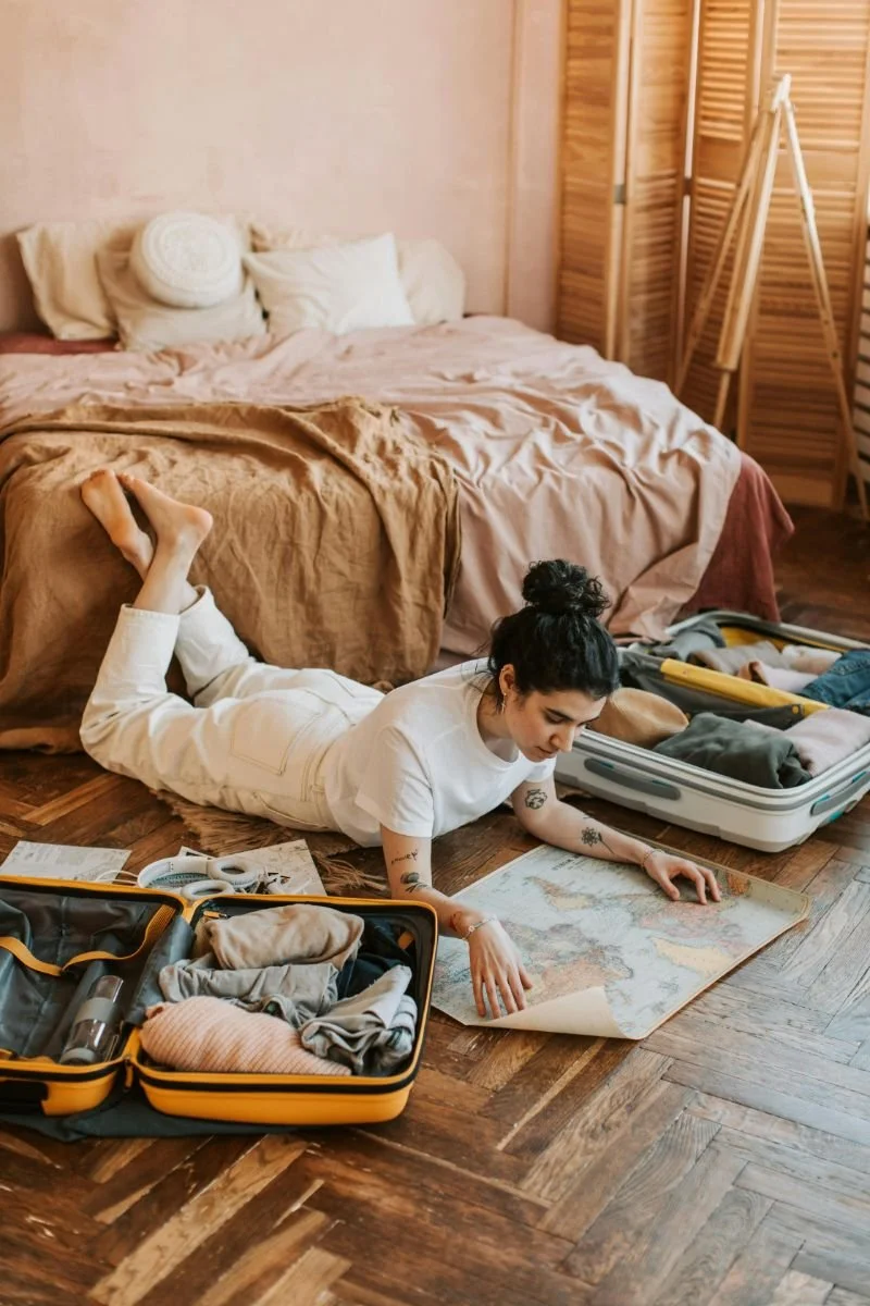 woman on floor with map and open suitcases next to her showing how planning and preparing for your much-needed time off can help you feel less guilt over taking time off work