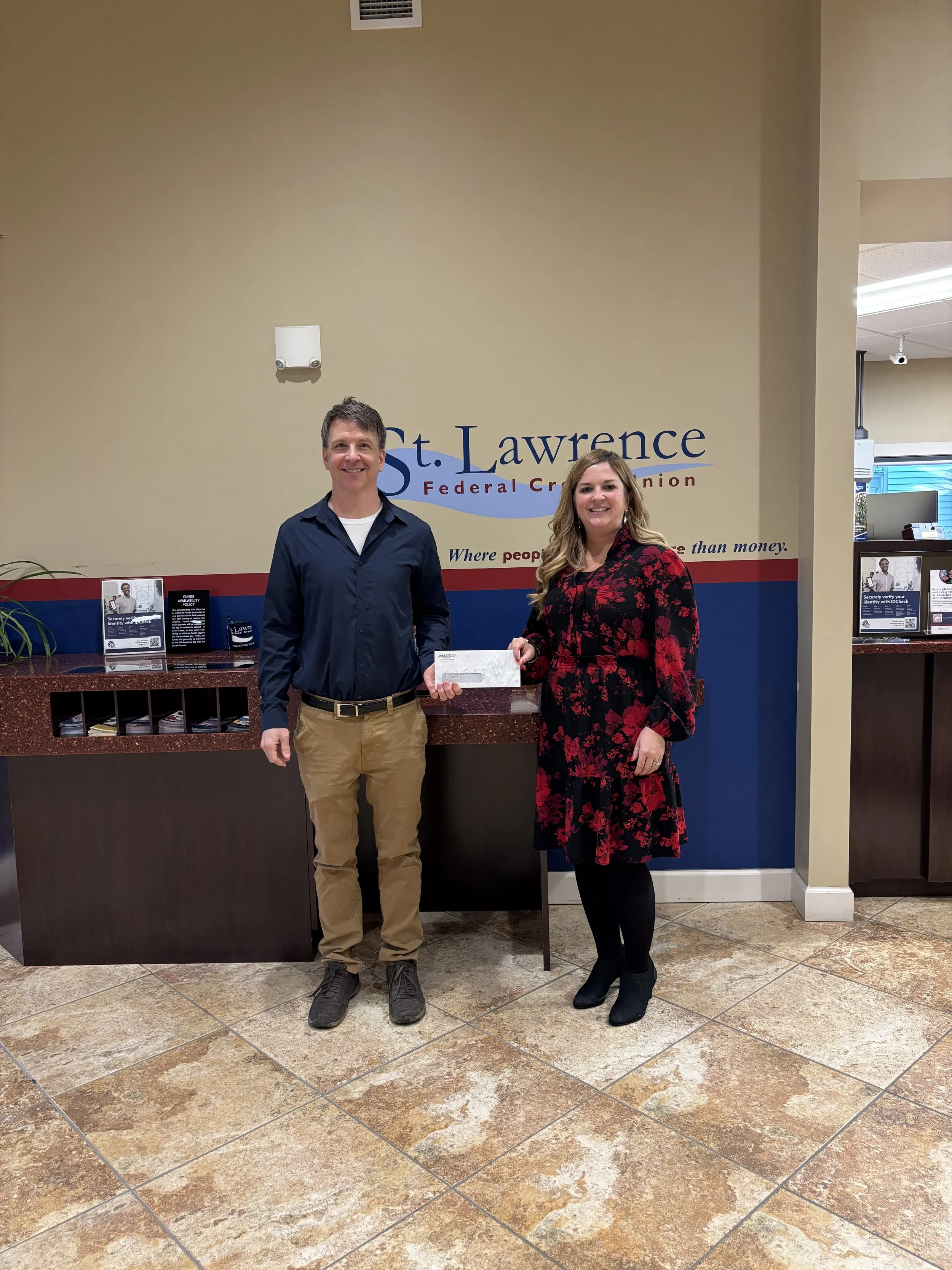 Adult male accepting a donation check from an adult female who works at the credit union.
