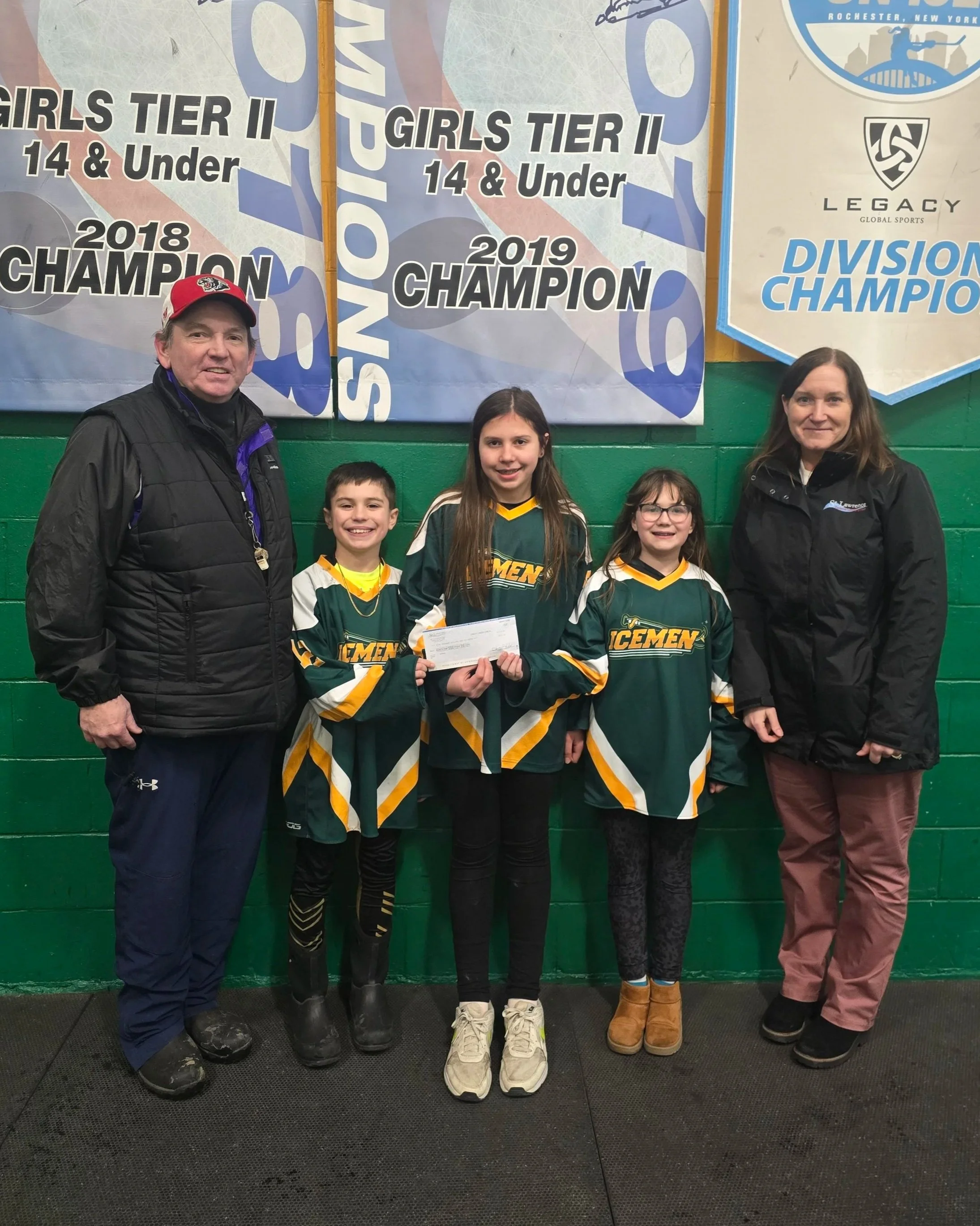 One adult female presenting a donation check to one adult male and three children for the Norwood-Norfolk Youth Hockey Association.