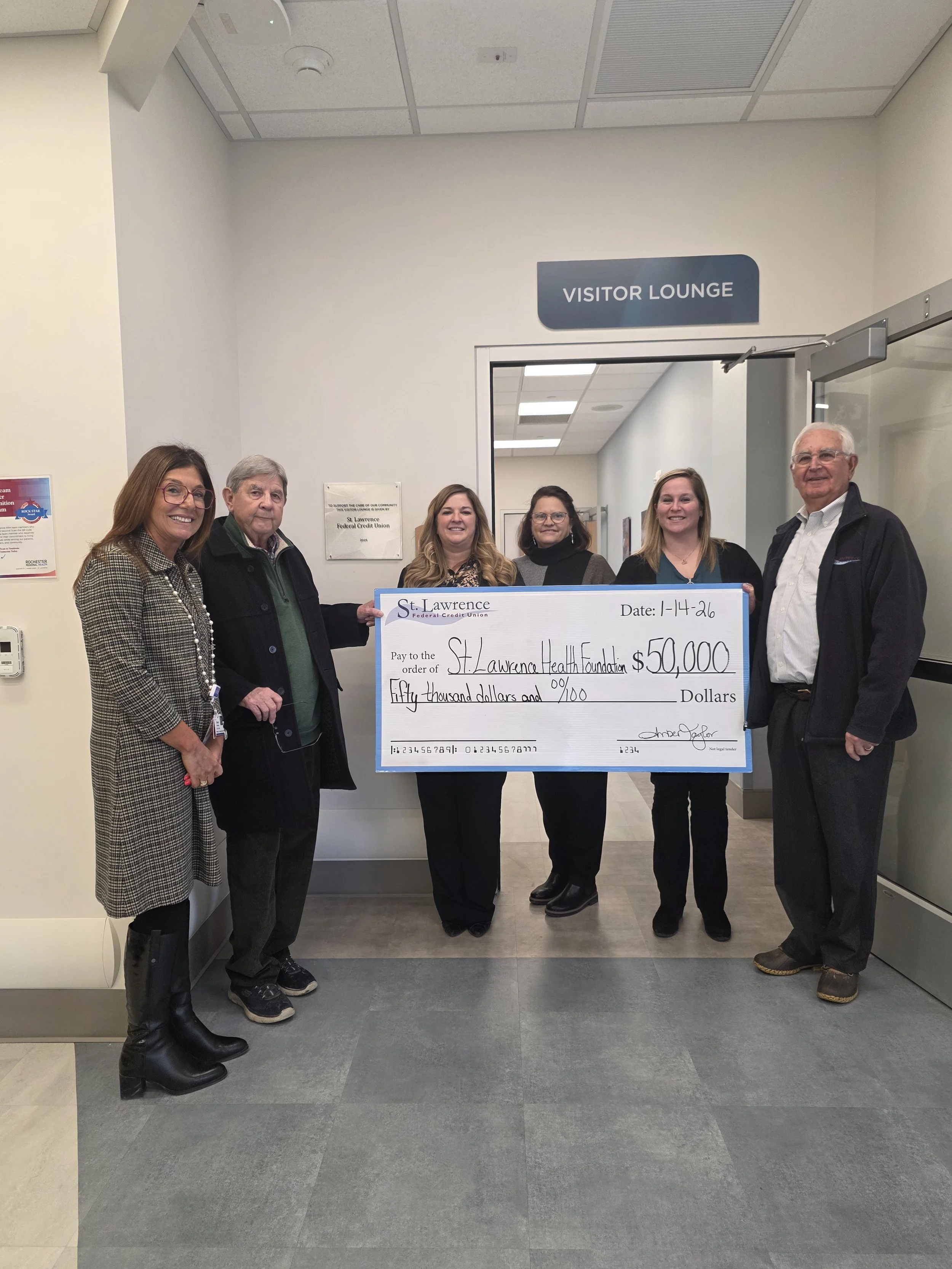 Three adult females and two adult males presenting a donation check to one adult female for the St. Lawrence Health Foundation.