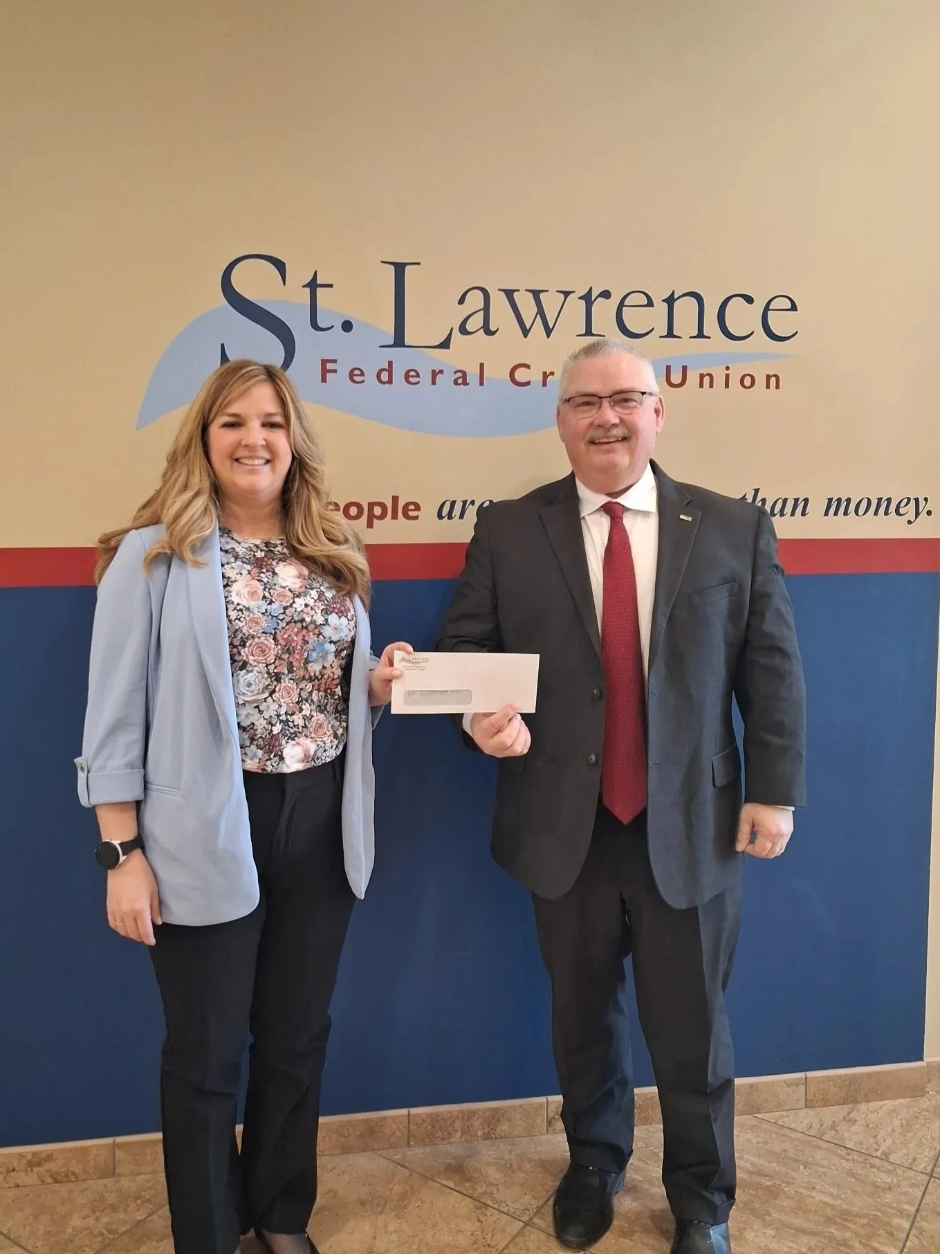 One adult female presenting a donation check to one adult male for the St. Lawrence Power and Equipoment Museum - Fort Tribute.