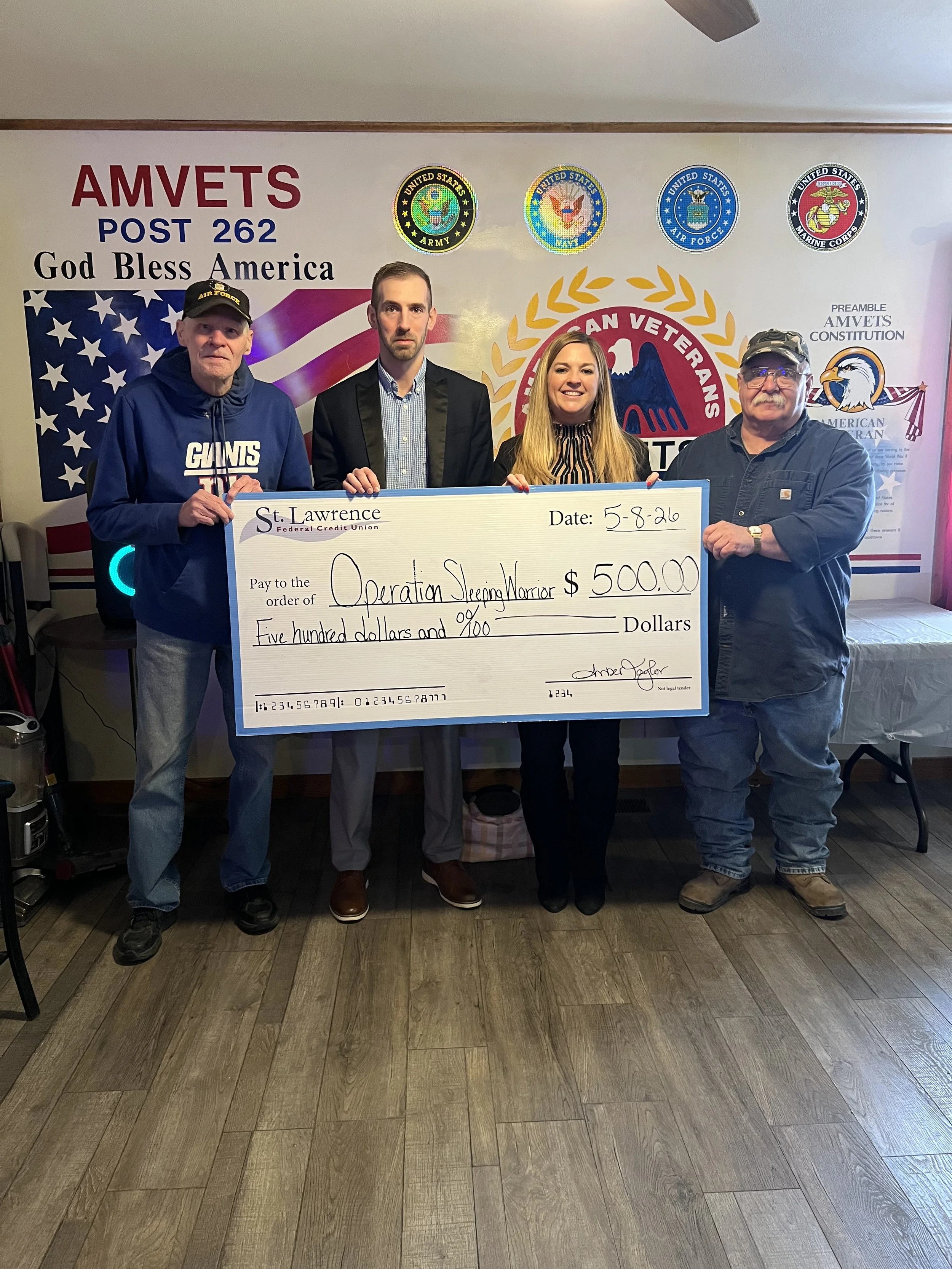 Two adult males accepting a donation check from an adult male and adult female in support of the Operation Sleeping Warrior Project. The check is oversized for the photo.