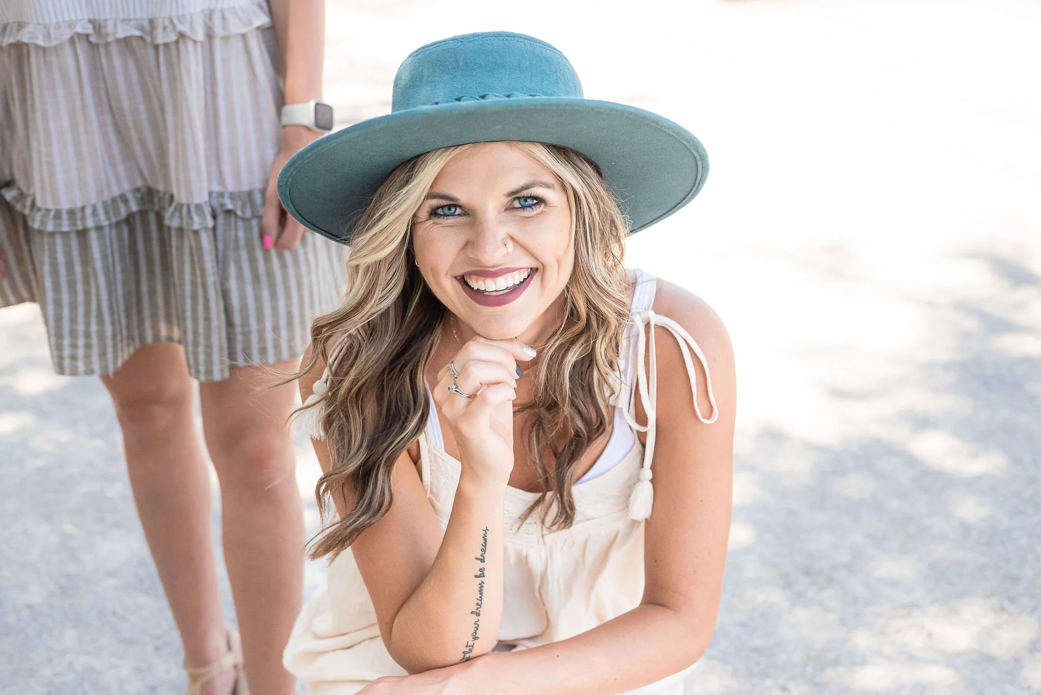 color image of influencer kneeling with hand under her chin and smiling, wearing a green hat