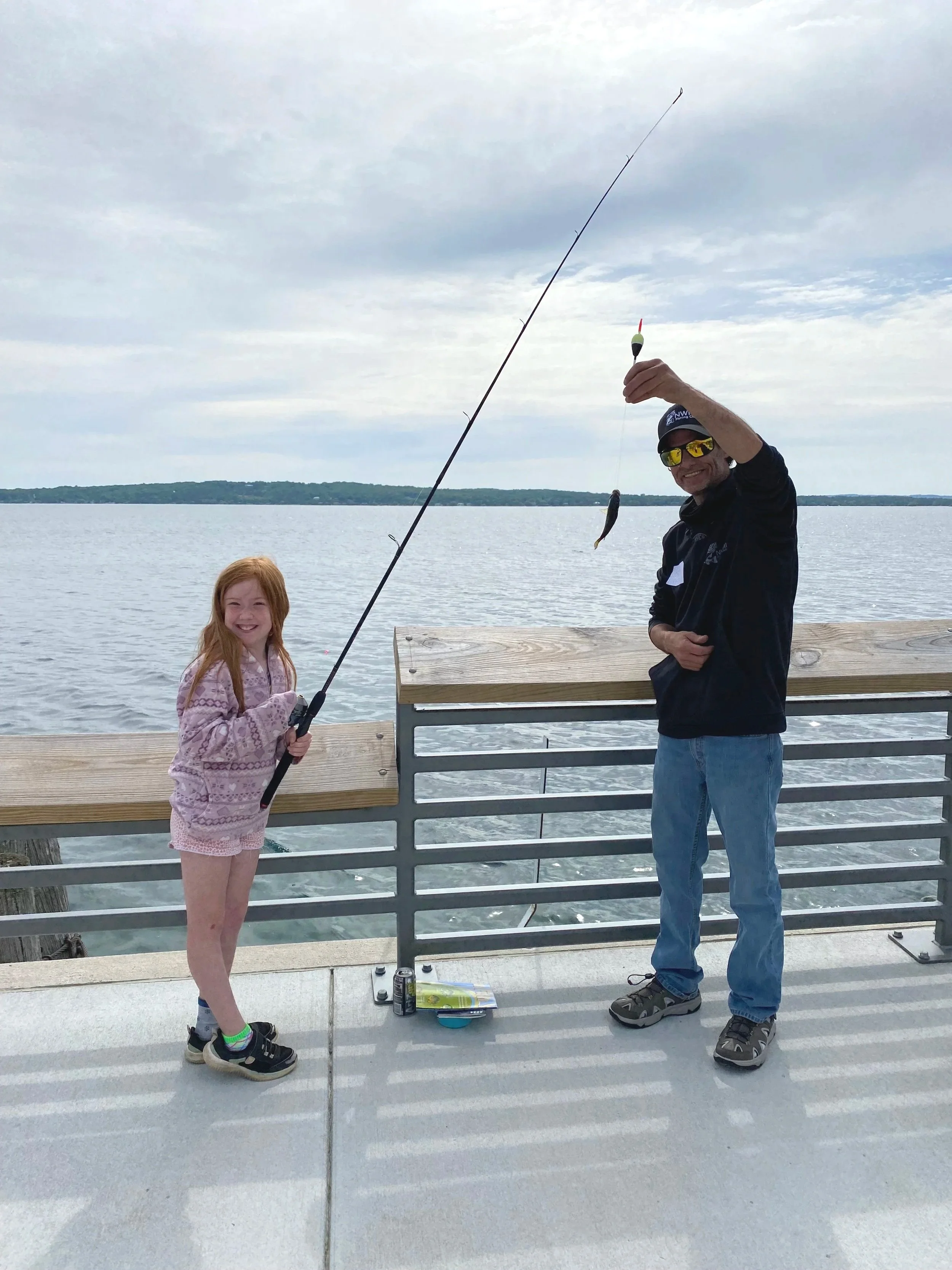 Volunteer holding a small fish beside a smiling girl in the pier fishing area