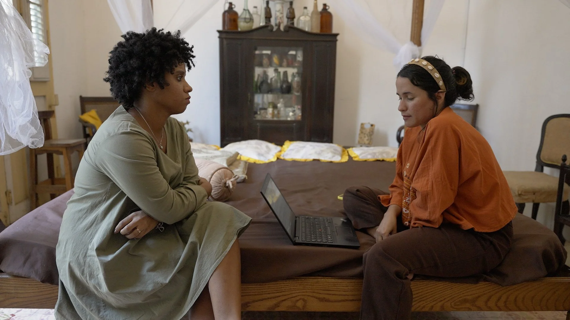 Claudia speaks with Belly of the Beast journalist Liz Oliva during an in-person interview, seated on a bed with a laptop between them.