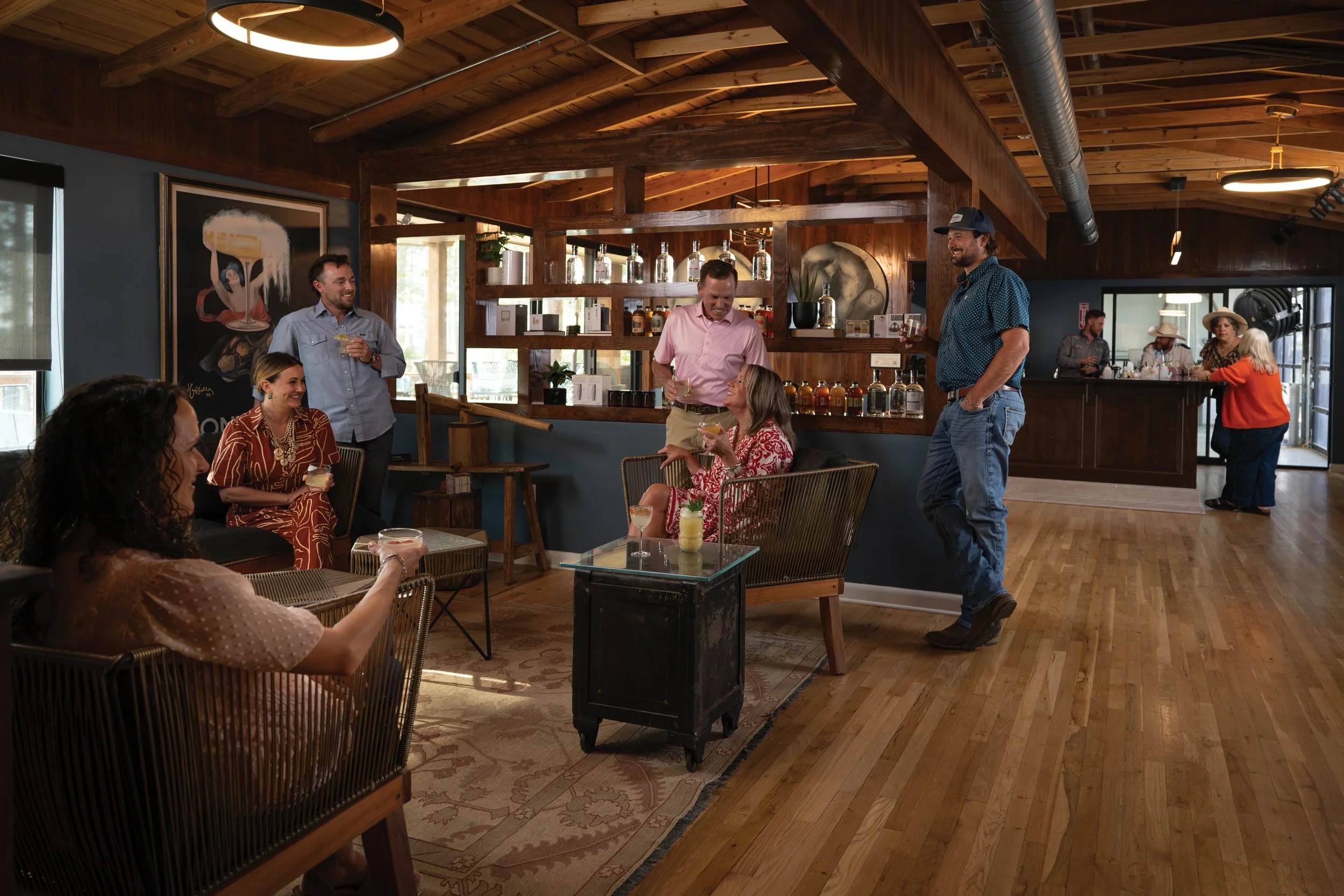 People socializing and enjoying drinks inside a cozy, wood-paneled bar or restaurant with artwork on the walls and a bar counter in the background.