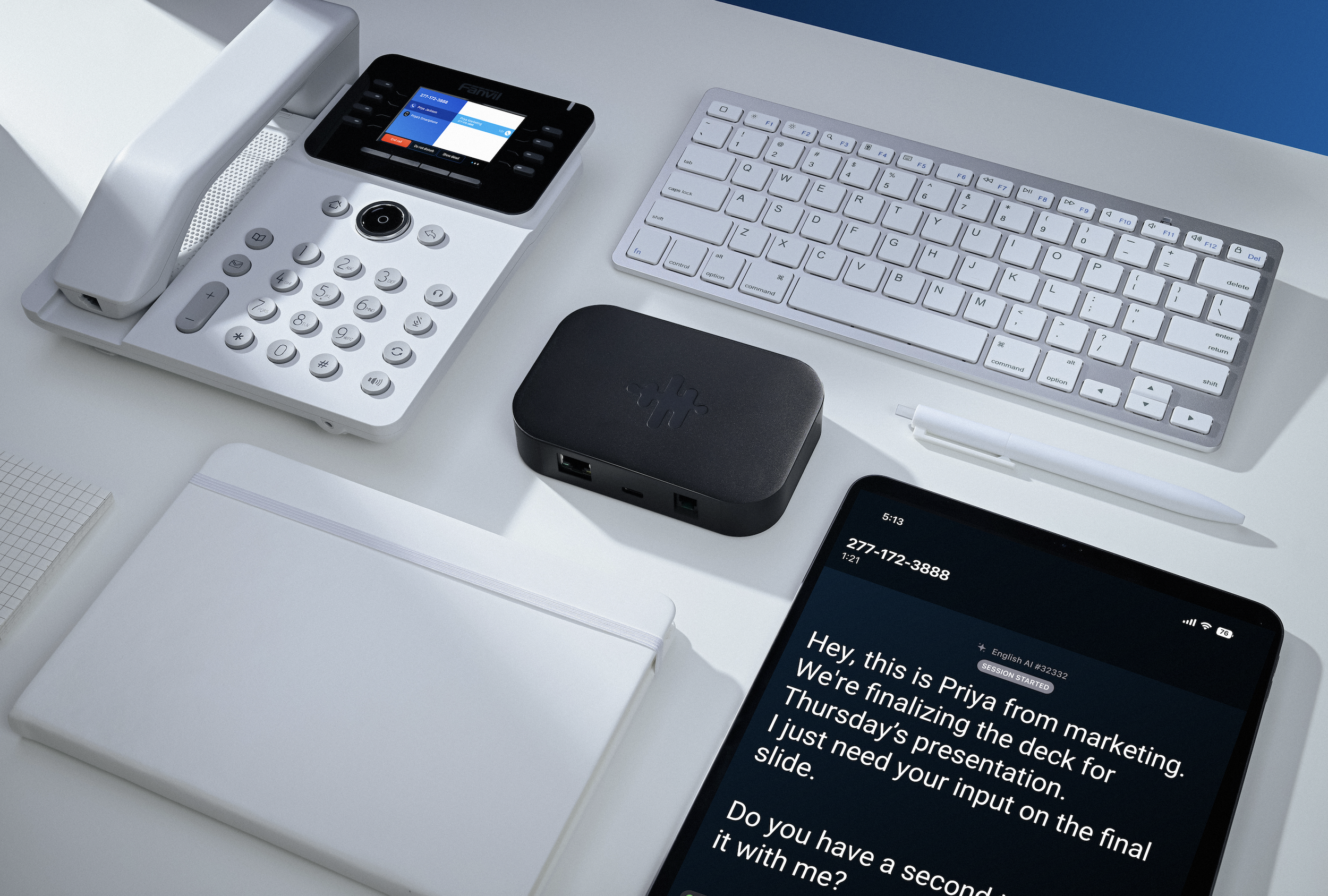 An overhead shot of a table with a keyboard, office phone, a tablet with captions on it and a black box (Bridge)
