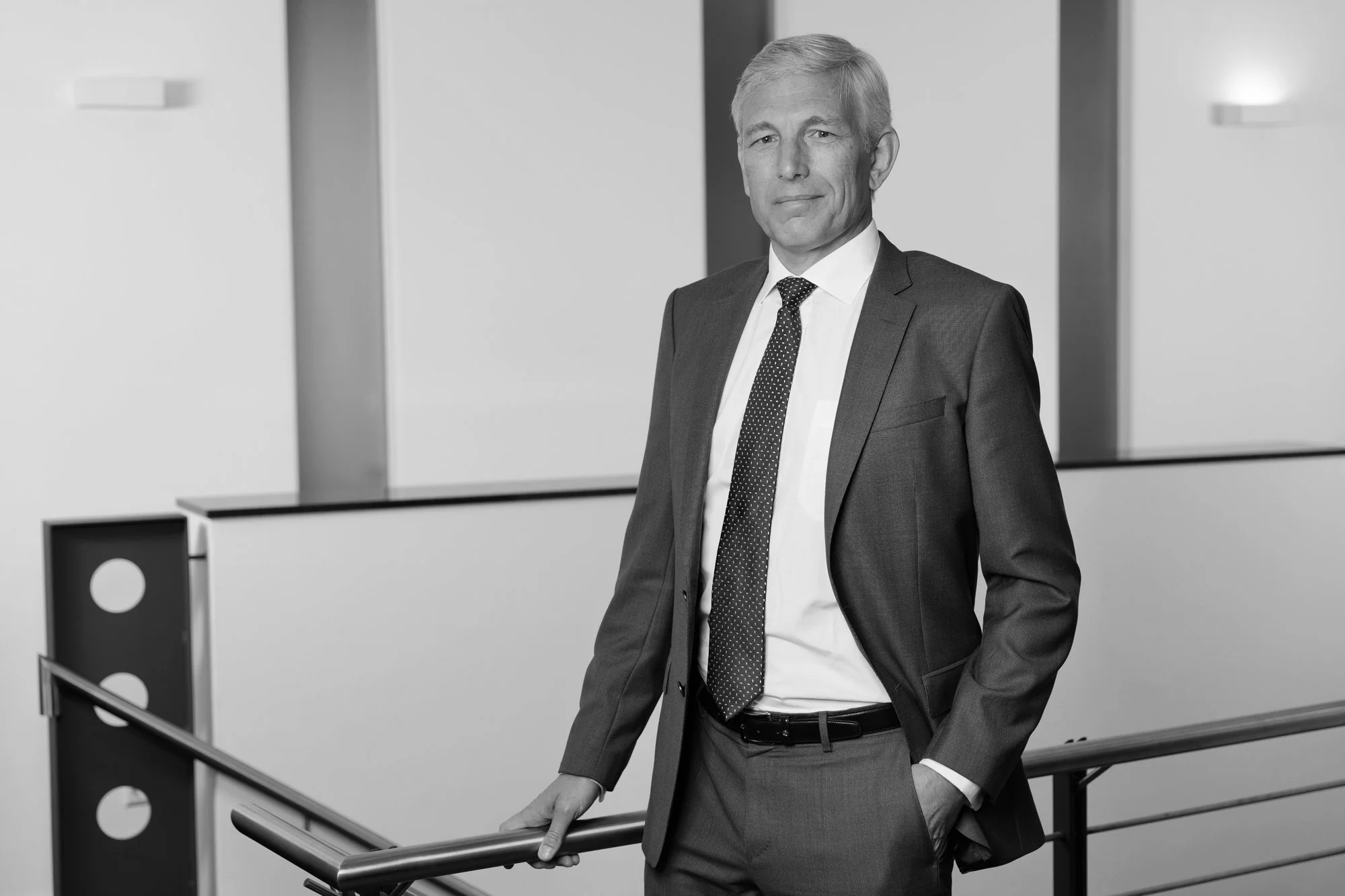 Mann in Businessanzug mit Hand auf Geländer, modernes Büro im Hintergrund, Schwarz-Weiß-Foto