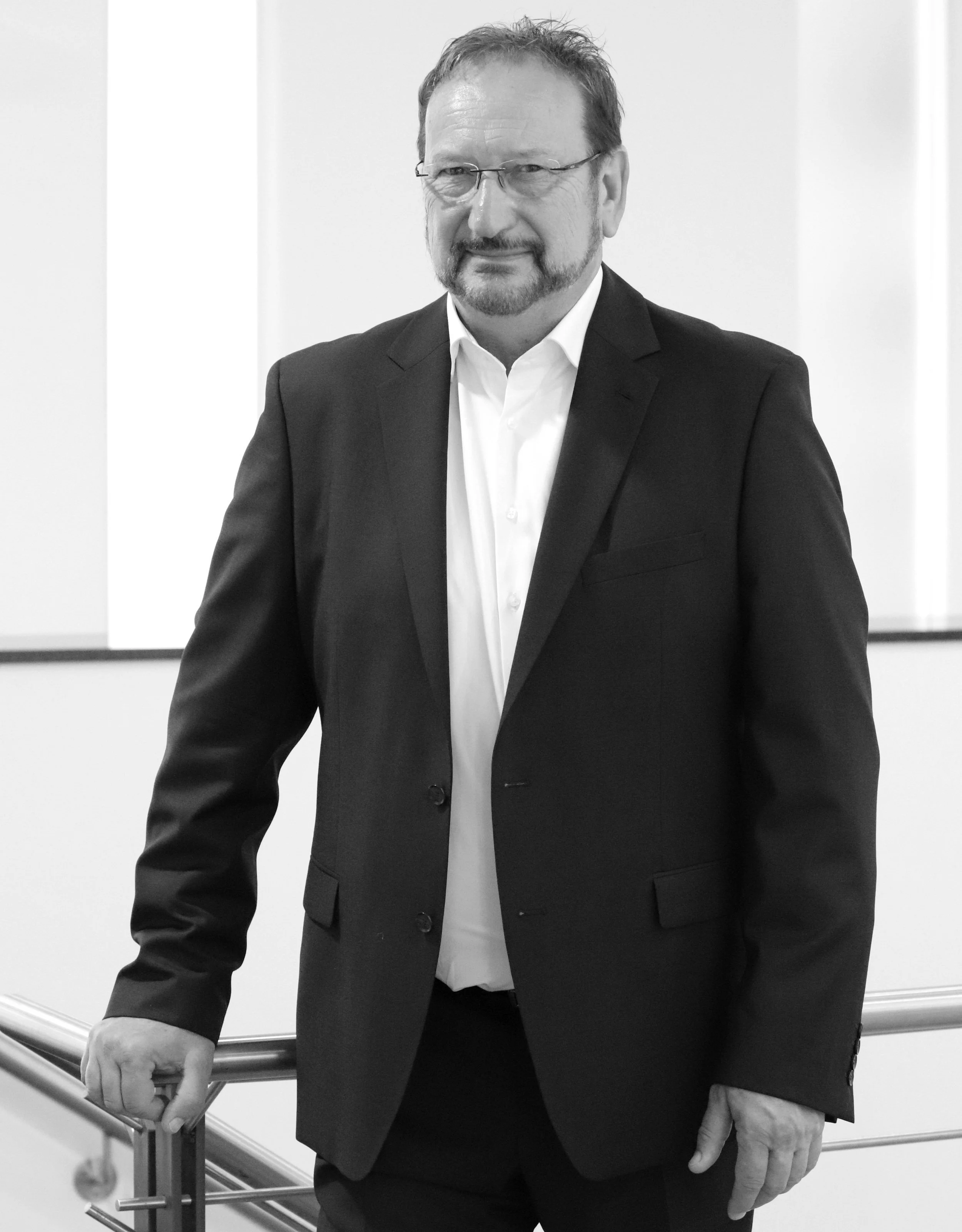 Schwarz-weiß-Foto eines Mannes in Anzug und Brille, der an einem Handlauf lehnt.