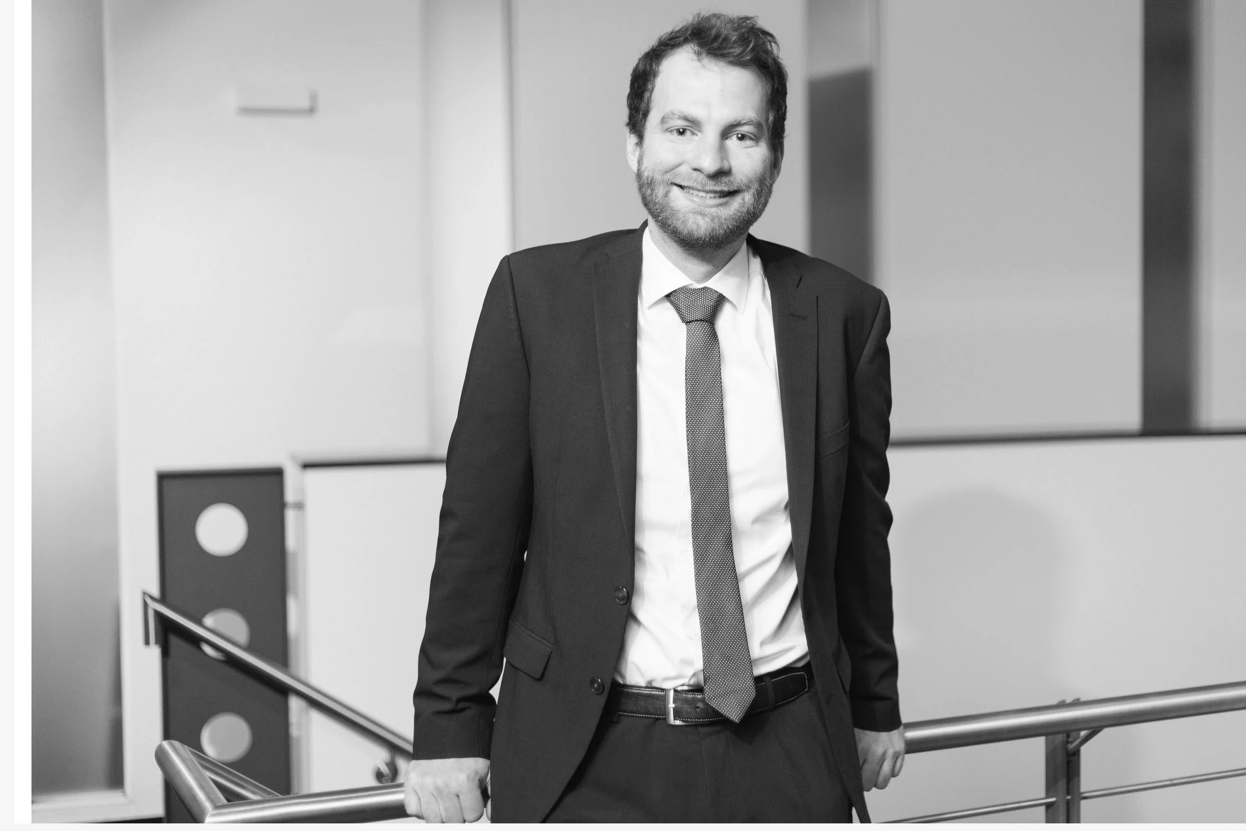 Ein lachender Mann in Geschäftsanzug steht an einer Treppe in einem Bürogebäude.