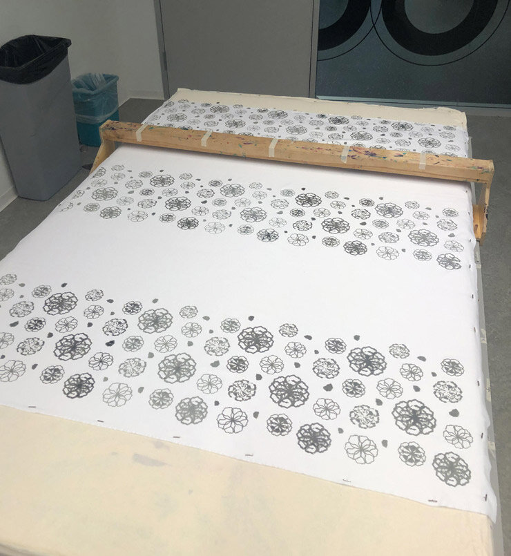 Sheet of paper with a pattern of black and white floral illustrations, held on a table with a wooden ruler diagonally placed on top, in a laundry room or similar setting.