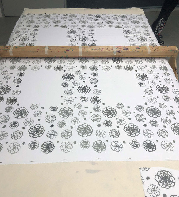 A large sheet of paper with a pattern of black floral designs, set on a flat surface with a wooden ruler across the top.