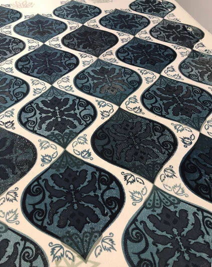 A close-up view of a decorative tile floor featuring blue and black ornate patterned tiles with a white border containing leaf designs.