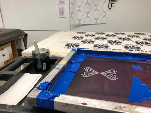 Screen printing setup with a squeegee, ink, and a design on a screen for printing. Blue tape on the edges of the screen.