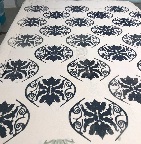 A white bedspread with a repeating black damask pattern.