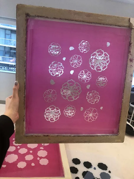 People holding a tray with pink paper featuring white floral cutouts, a larger floral pattern in the middle and smaller floral patterns around it.