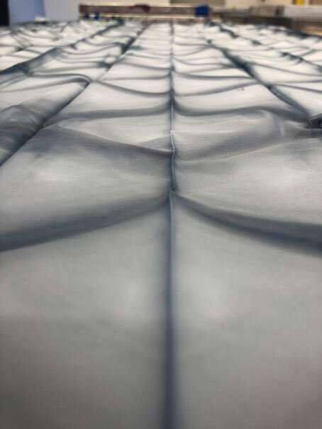 Close-up view of multiple gray, quilted cushions or mattresses arranged in rows.