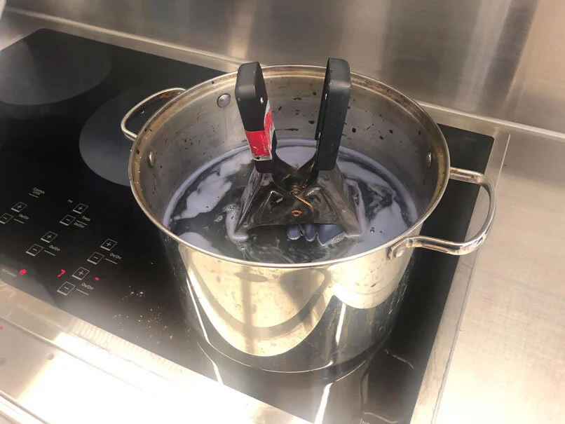 Pot on stove with black tongs inside, boiling a dark liquid.