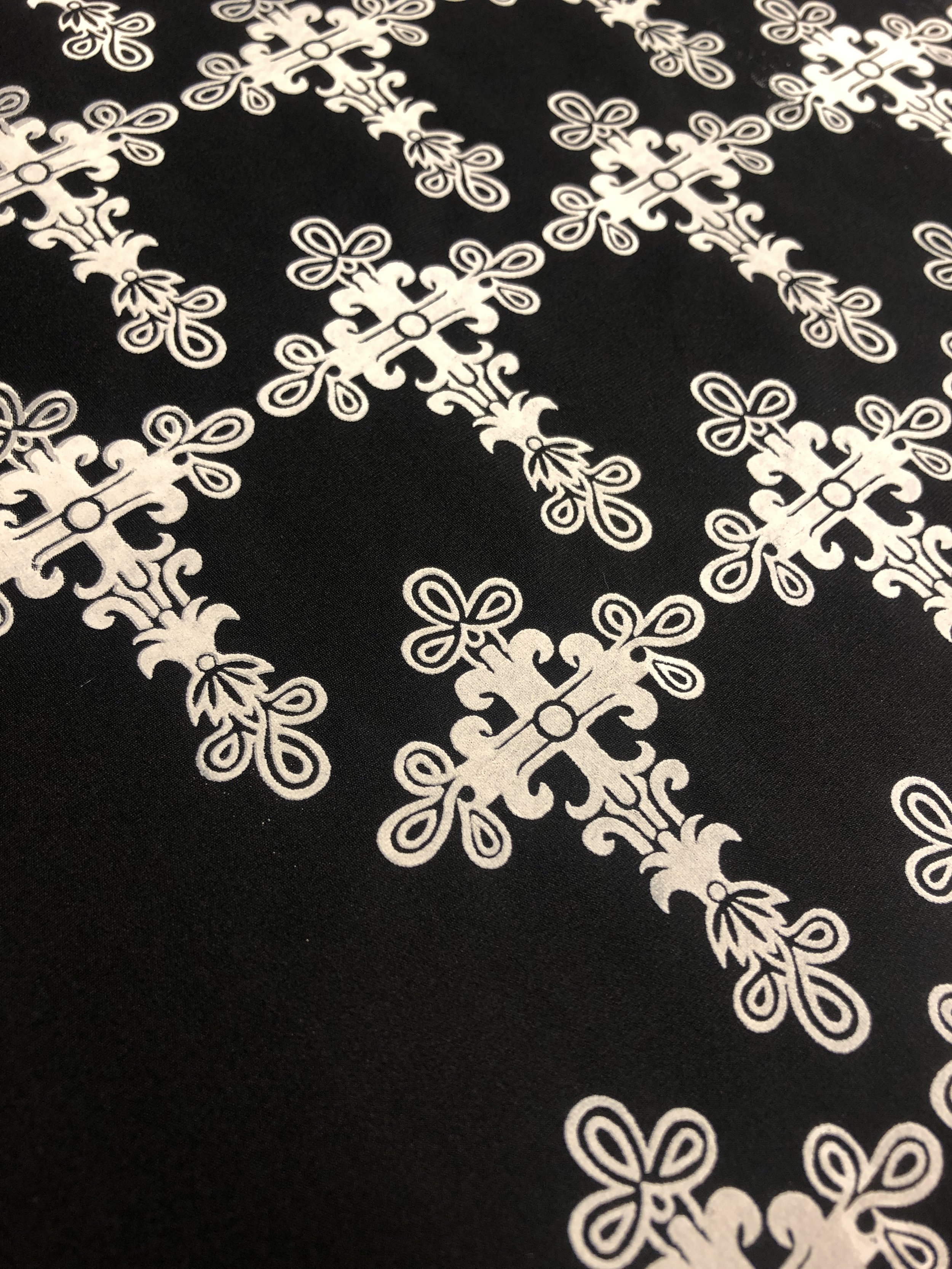 Close-up of a black fabric with white ornate floral and geometric patterns, creating a decorative border design.