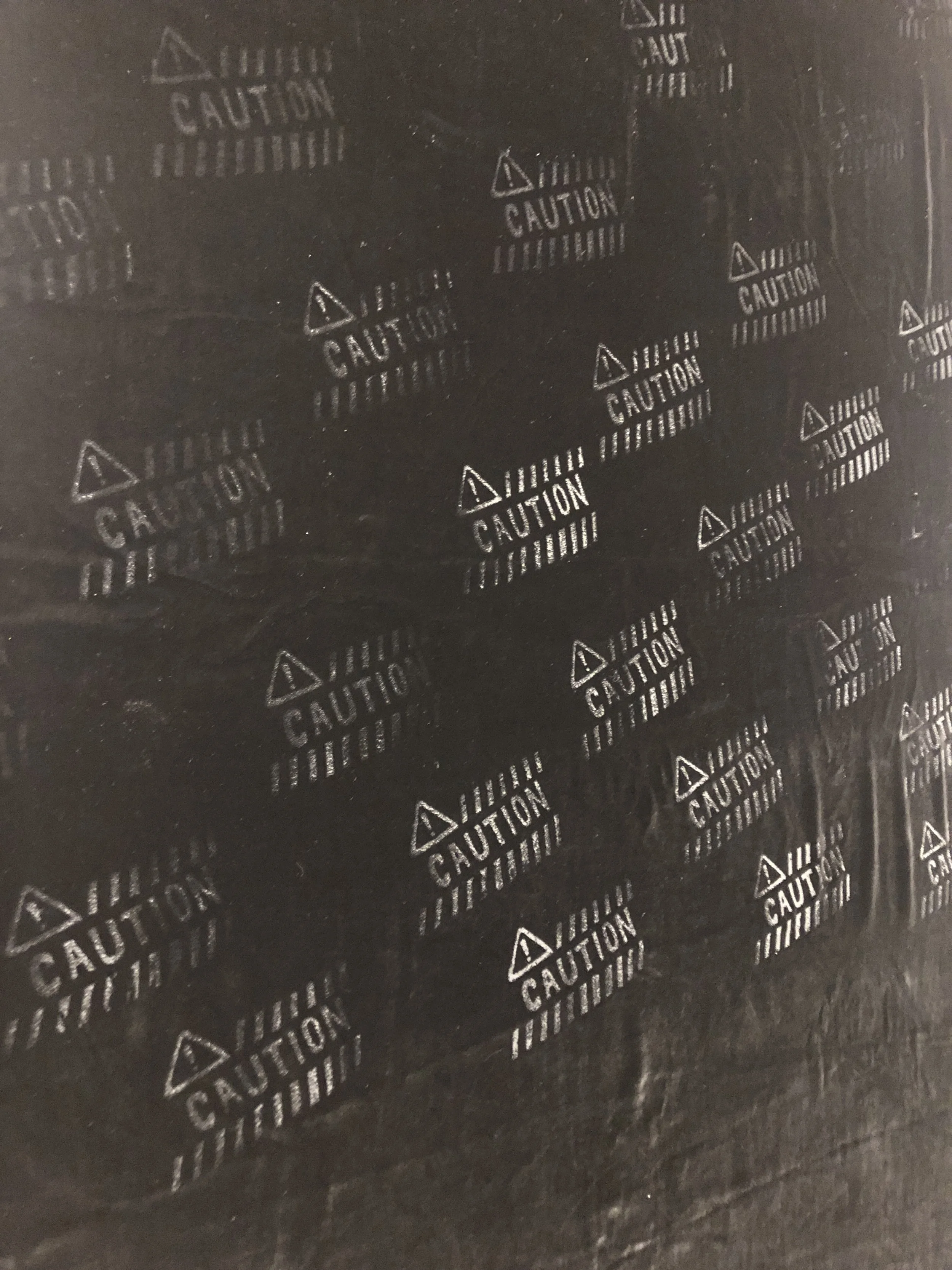A roll of black protective film with the word 'CAUTION' printed repeatedly in white, along with a triangle warning symbol.
