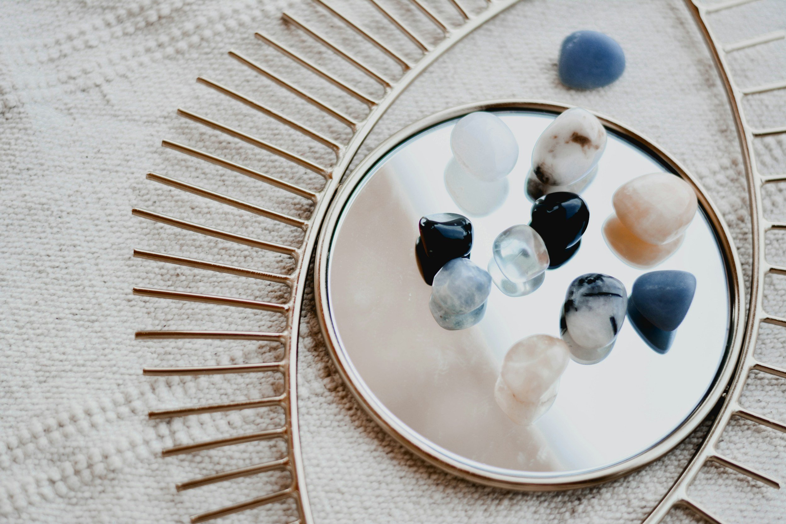 Collection of various rocks and stones on a round mirror plate with a decorative gold-colored metal frame, placed on a textured beige fabric surface.