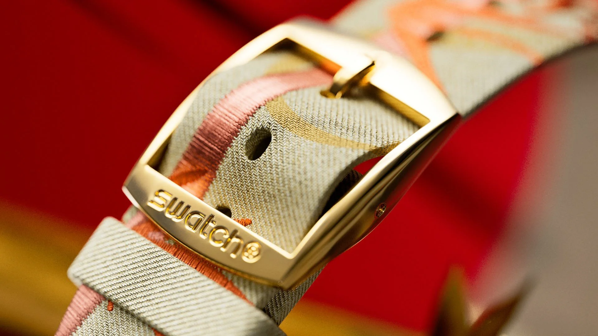 Close-up of a patterned fabric watch strap with a gold buckle engraved with the word "Swatch".