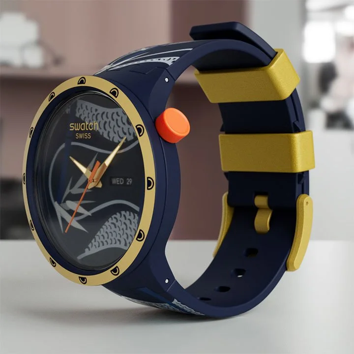 A blue and yellow Swatch Swiss smart watch with a round face displaying the time and date, sitting on a white surface.