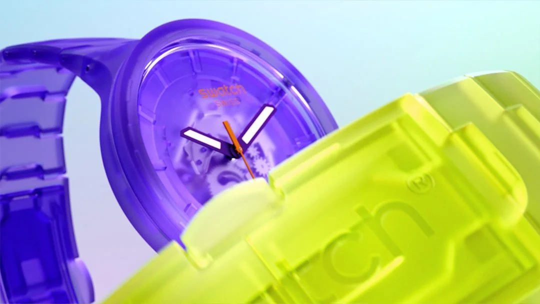 Close-up of colorful translucent watches, mainly purple and yellow, with minimalistic designs against a gradient background.