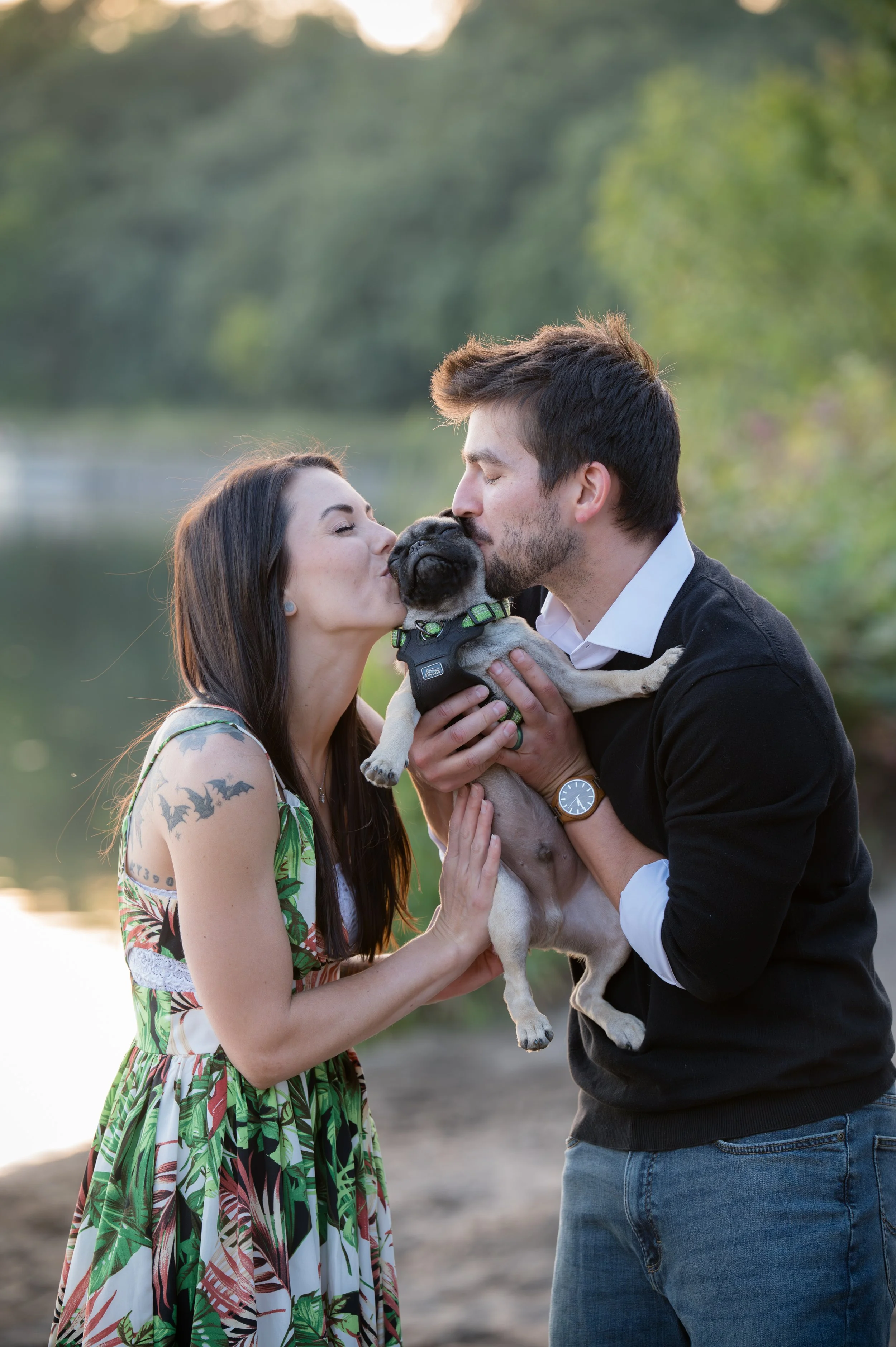 Romantic couple snuggles their Pug puppy and gives him kisses during an engagement session