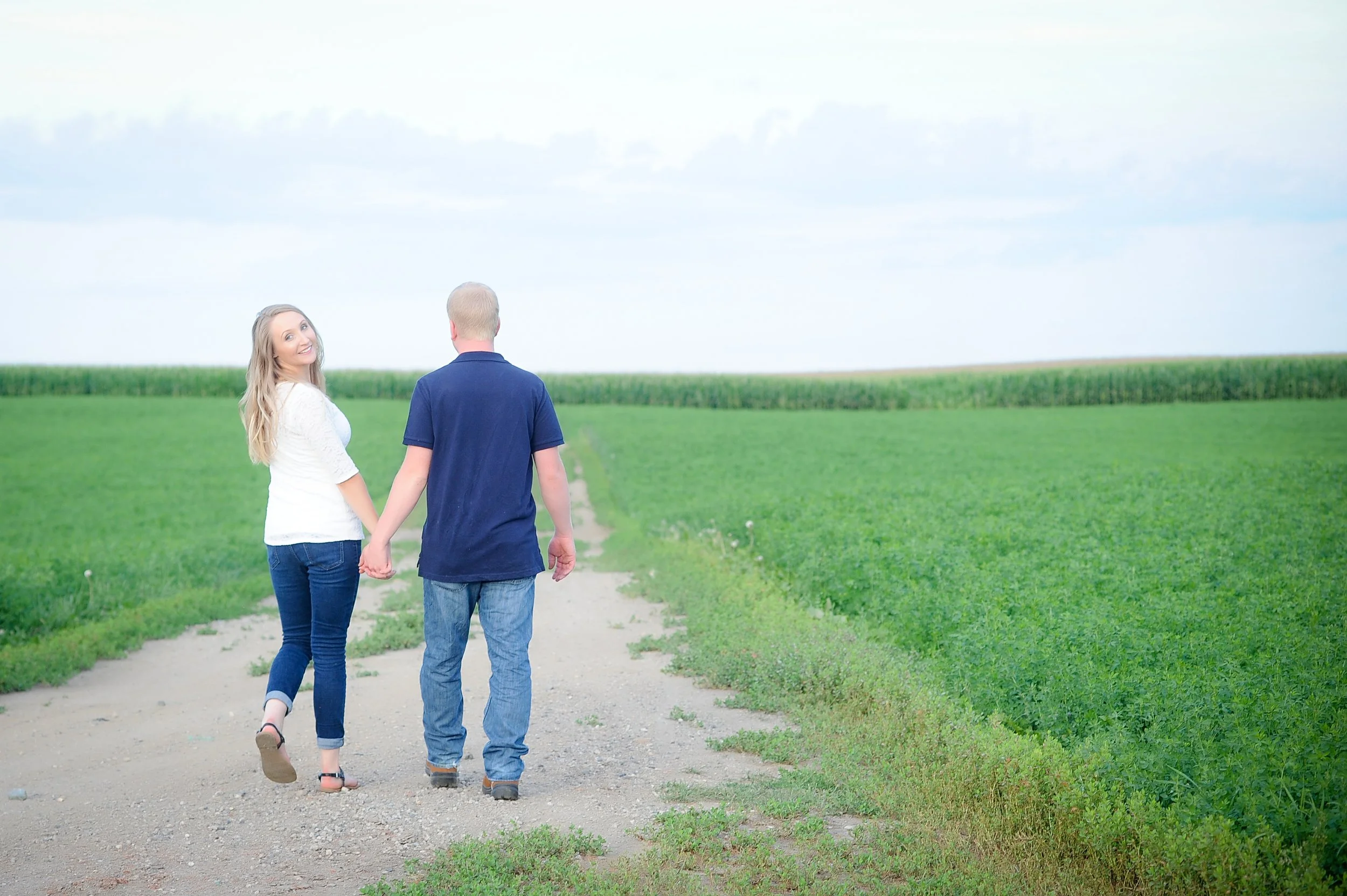 engaged couple walks hand in hand down a rural road in natural light