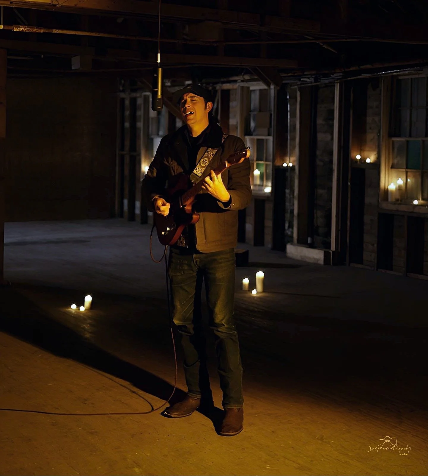A man singing and playing an electric guitar in a dimly lit room decorated with candles.