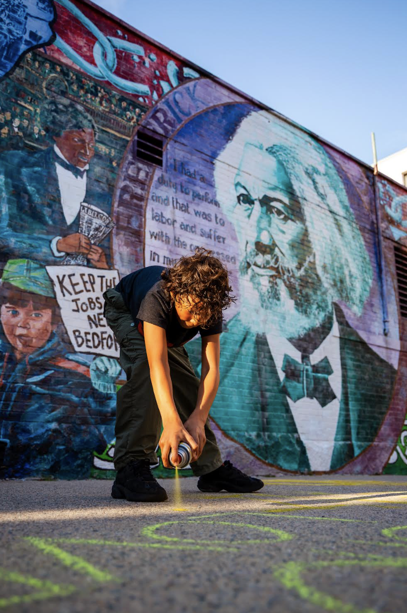 Child spraypainting in front of the Fredrick Douglas Mural