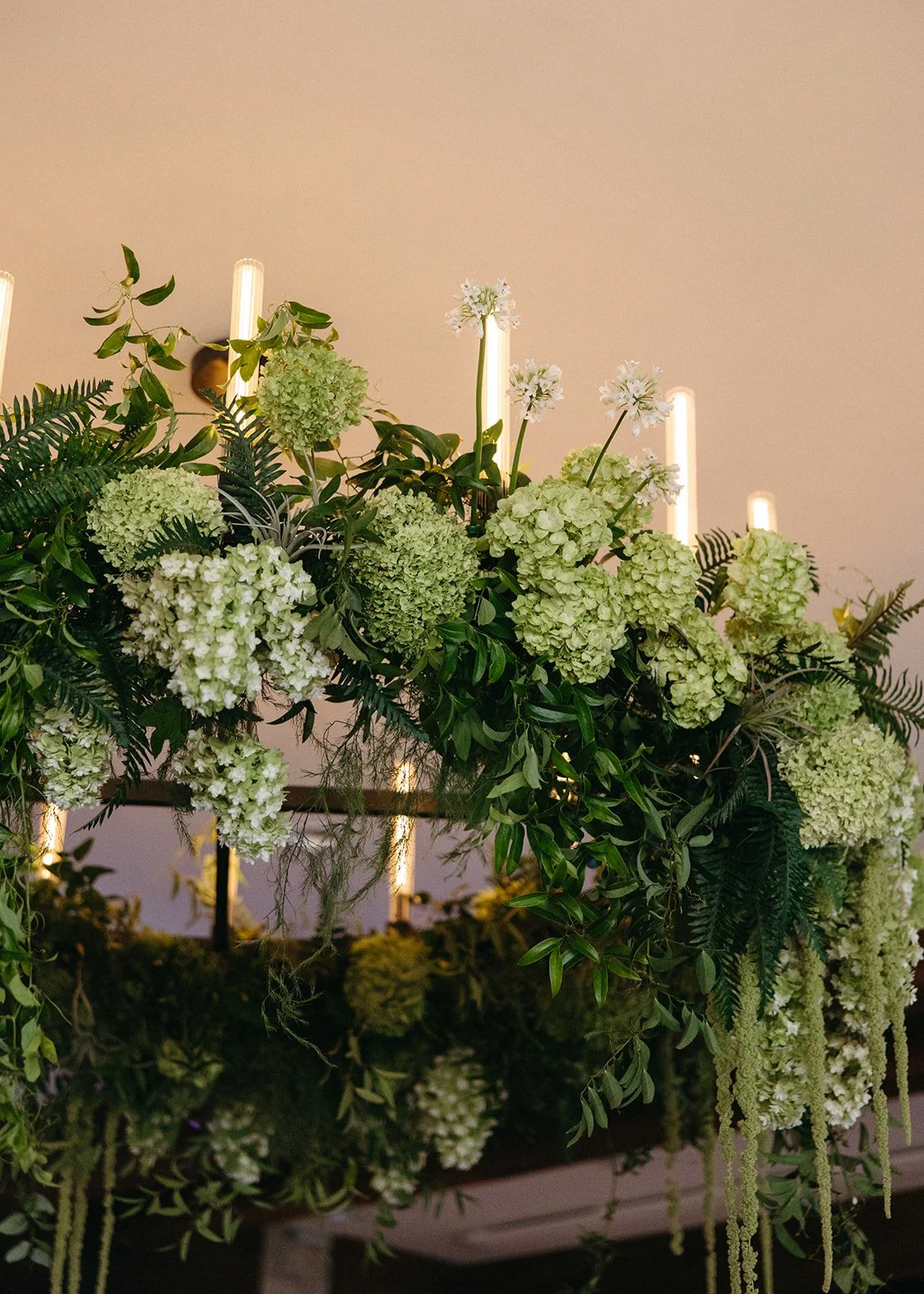 Hanging floral arrangement with green hydrangeas and ferns under ceiling lights.