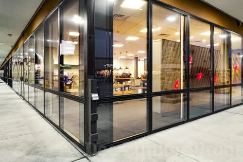 Exterior view of a modern glass-walled storefront or restaurant with visible interior lighting and furnishings.