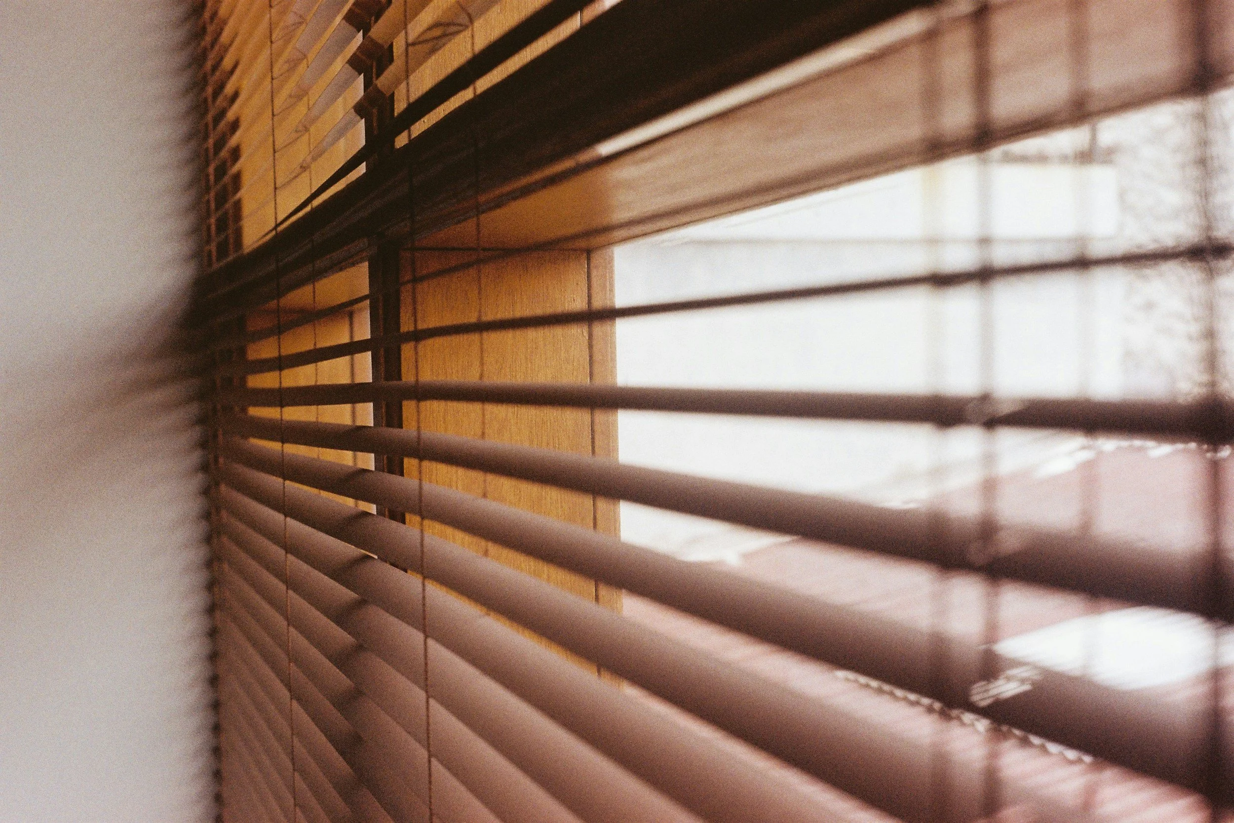 Close-up of wooden window blinds partially open, revealing a blurred outdoor scene.