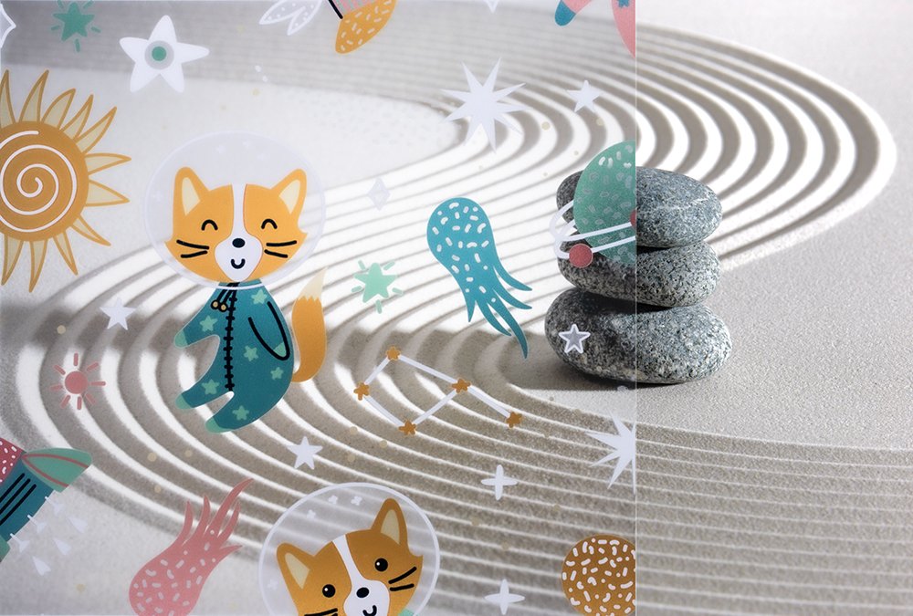 Decorative sand garden with three stacked stones, paper illustrations of cats, jellyfish, stars, the sun, and other sea creatures, on a surface with sand patterns.