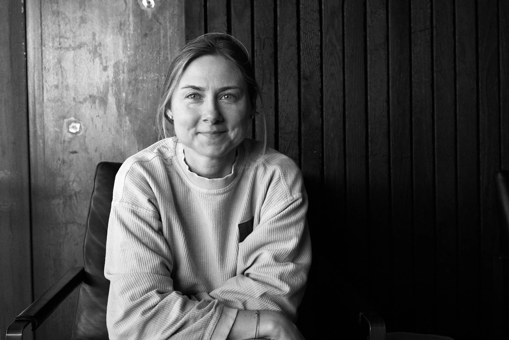 Katie Read, Psychotherapist smiling and sitting in a chair in a room with wood-paneled walls. The photo is in black and white.