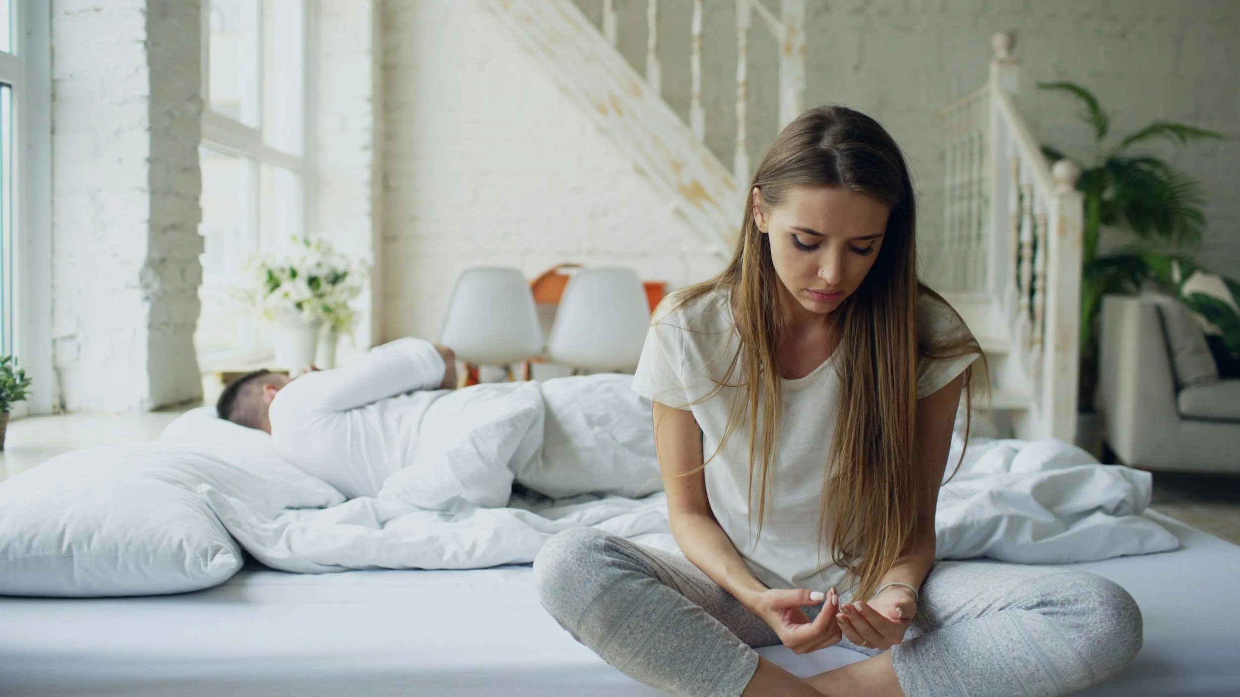 woman sitting on edge of bed looking down and distressed.