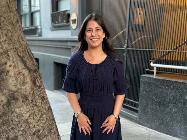 Simran standing outdoors in city by tree smiling