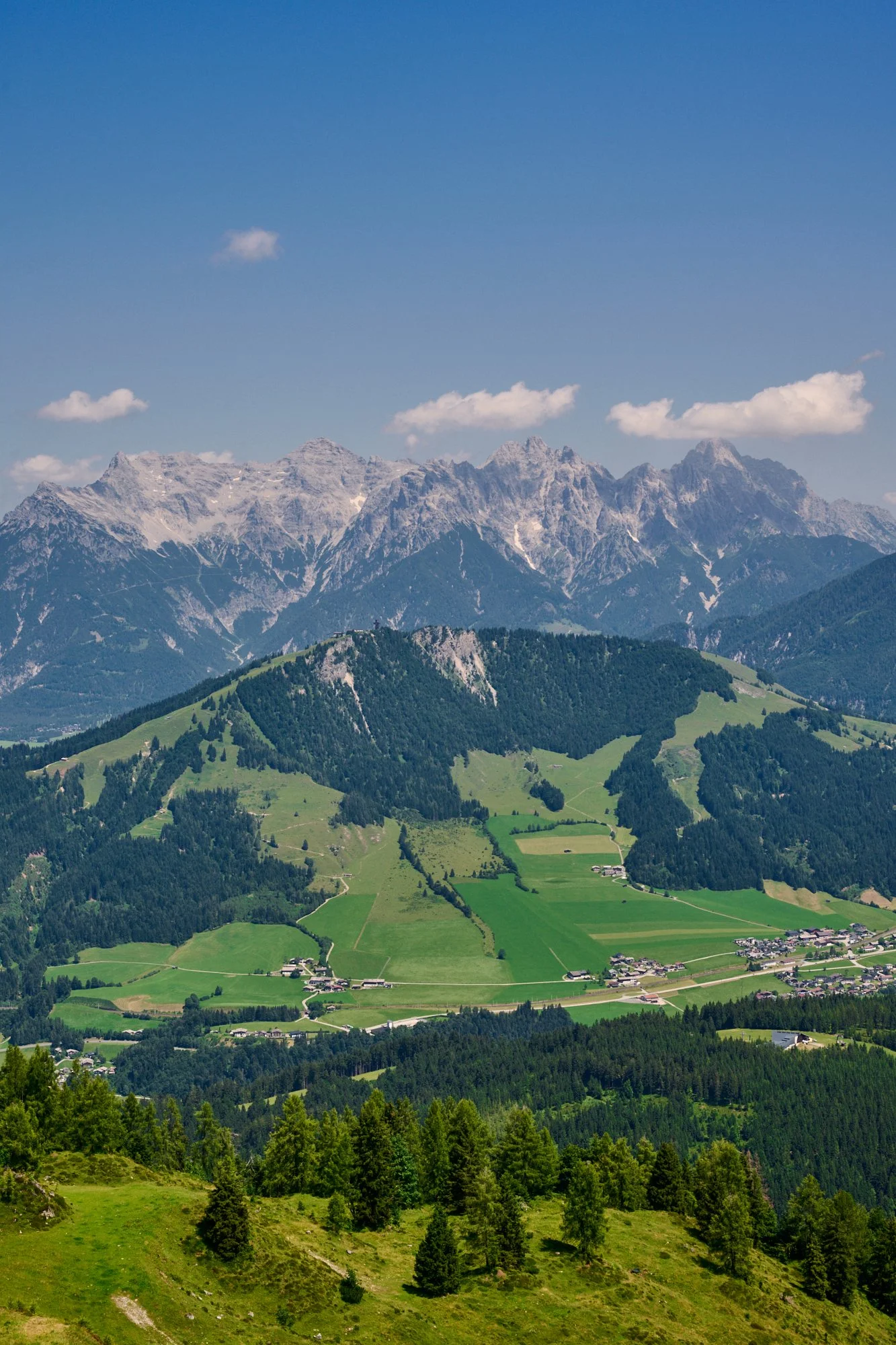 Scenic view of green hills and alpine mountains against a blue sky with scattered clouds.