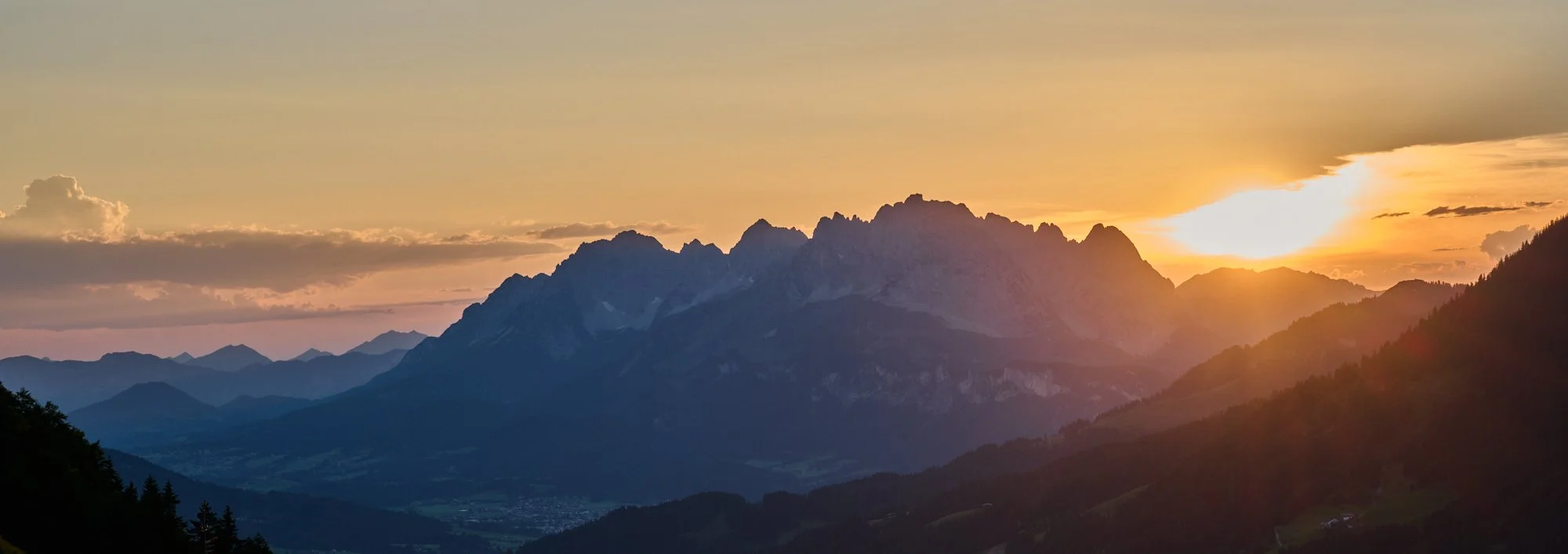 Sunset over a mountain range with layered peaks and a valley below.