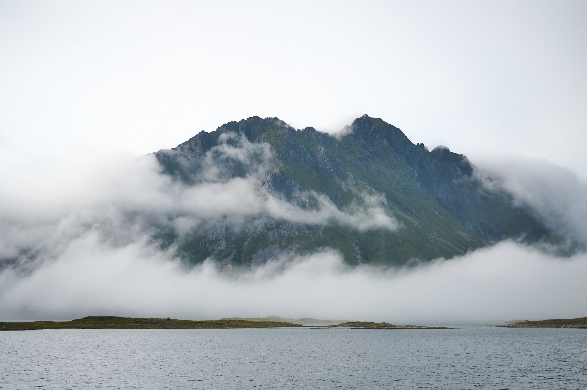 A mountain partially covered with clouds reflected in a body of water at its base.